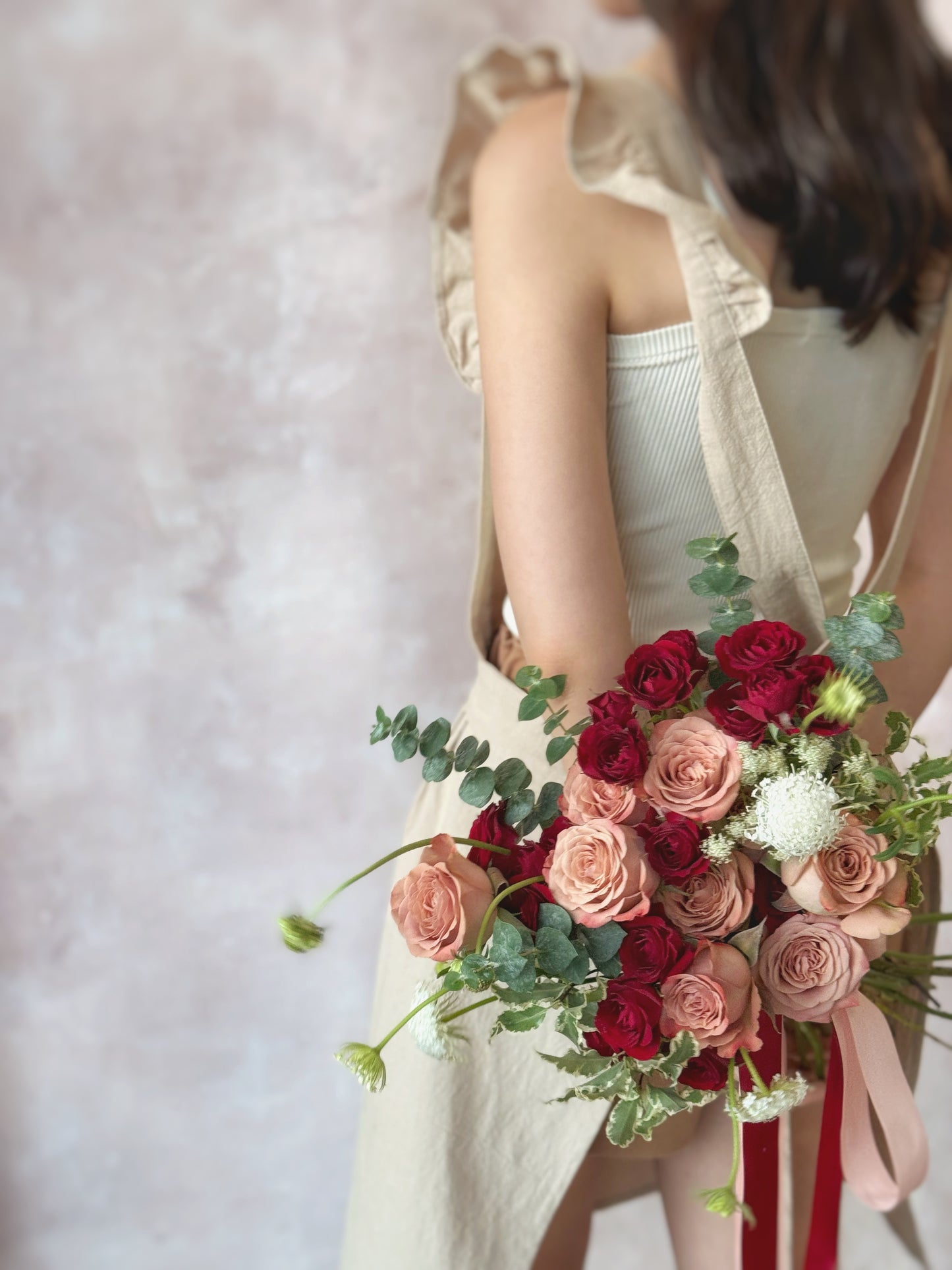 Romantic wedding bouquet with deep red, maroon, and soft nude pink florals, including red spray roses and cappuccino roses, held by a model at the back