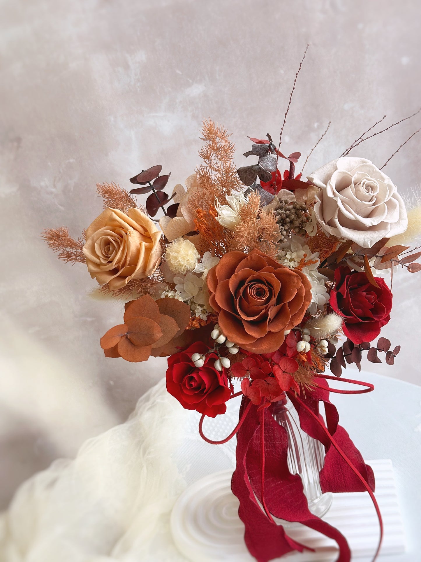 A close-up of the bouquet’s fiery autumn hues, featuring red and rusty orange roses with delicate floral textures.
捧花特写,火红与铁锈橙色玫瑰交织,呈现秋意盎然的细腻花卉层次。