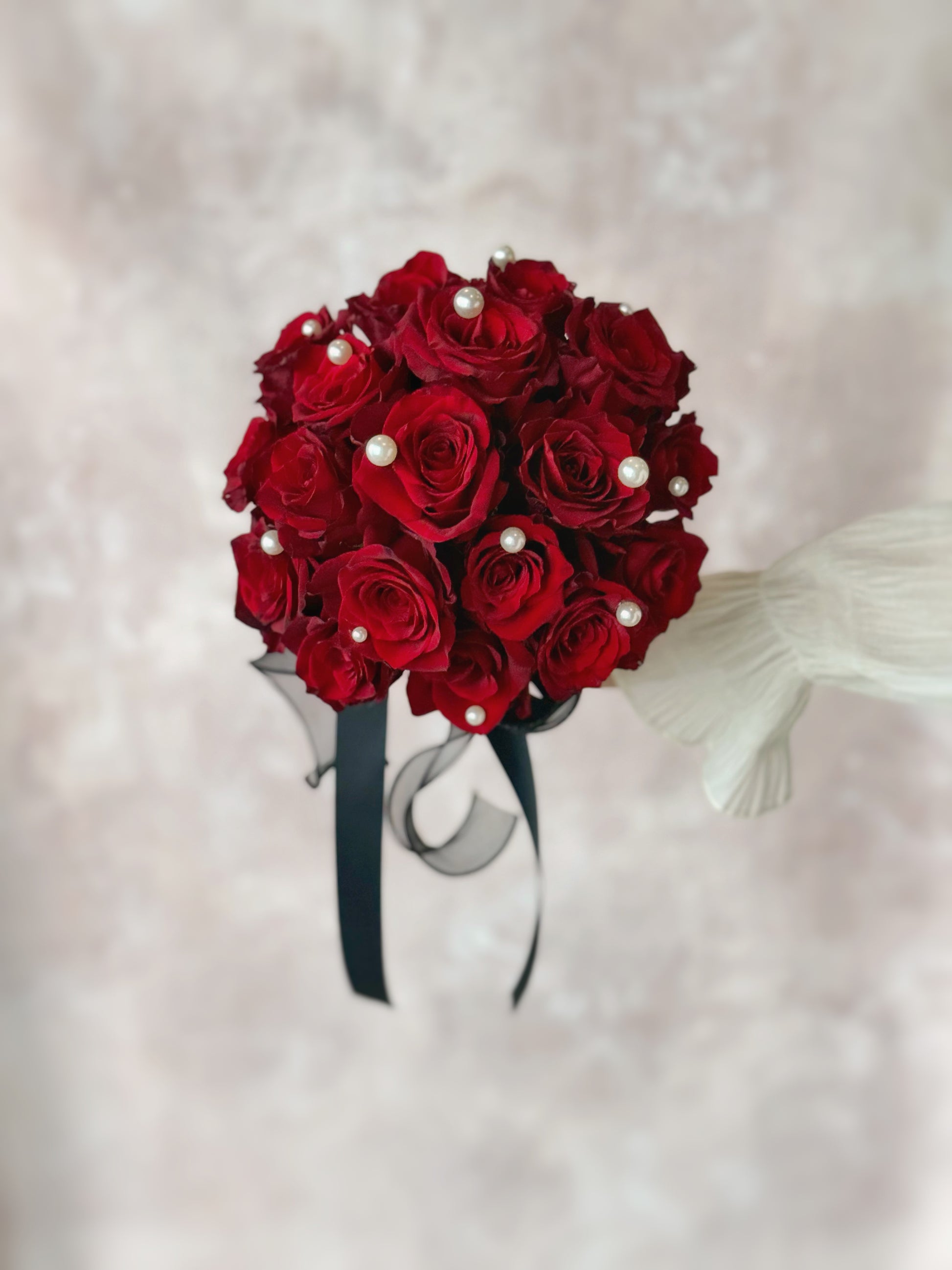 Detailed view of a maroon bridal bouquet, showcasing lush roses, shimmering pearls, and a statement black ribbon
