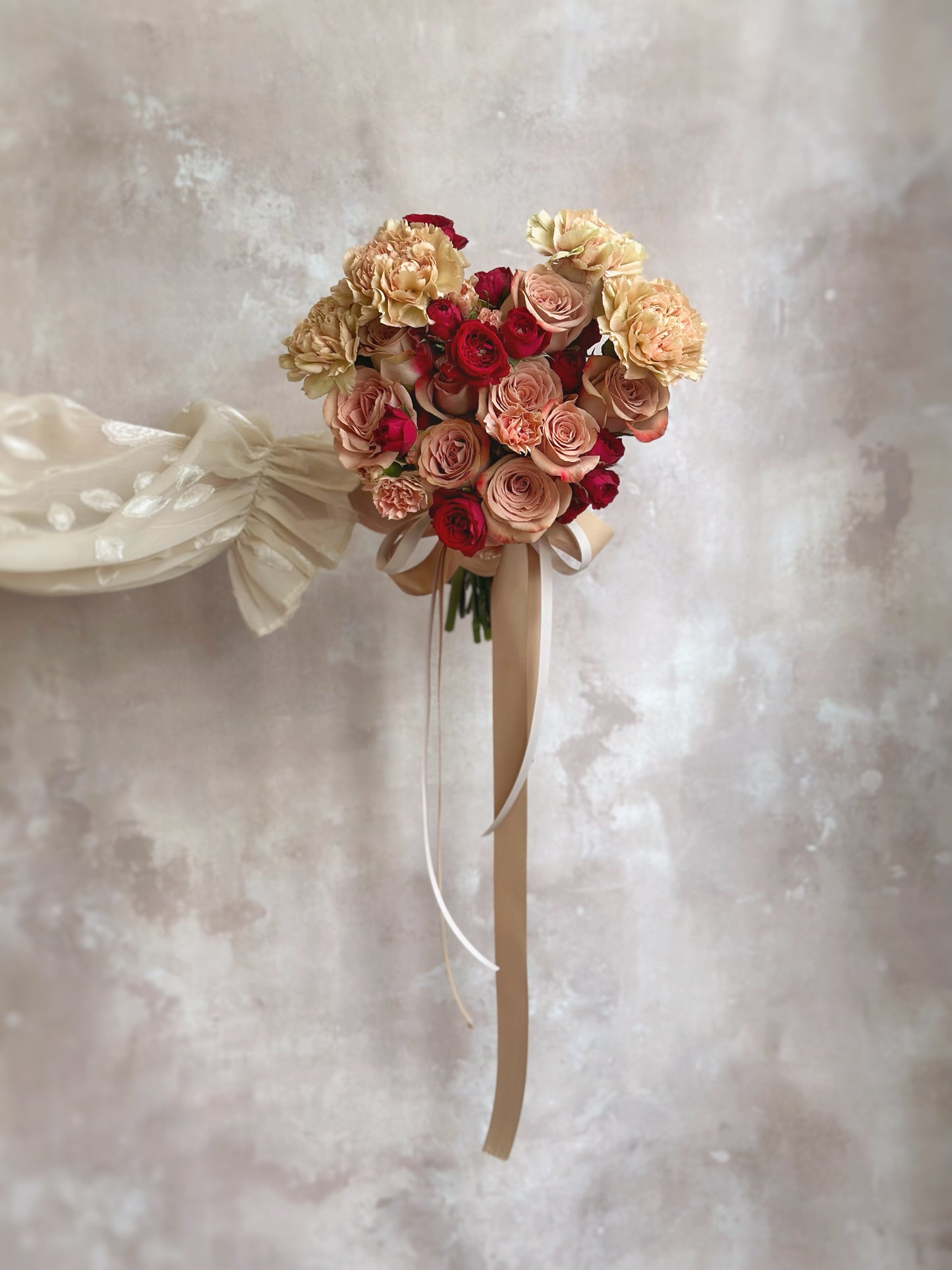 A bride delicately holding a heart-shaped bouquet, with cappuccino pink and maroon red flowers forming a stunning symbol of love.
新娘手持心形捧花,卡布奇诺粉色和深酒红花朵交织,展现令人惊艳的爱情象征。
