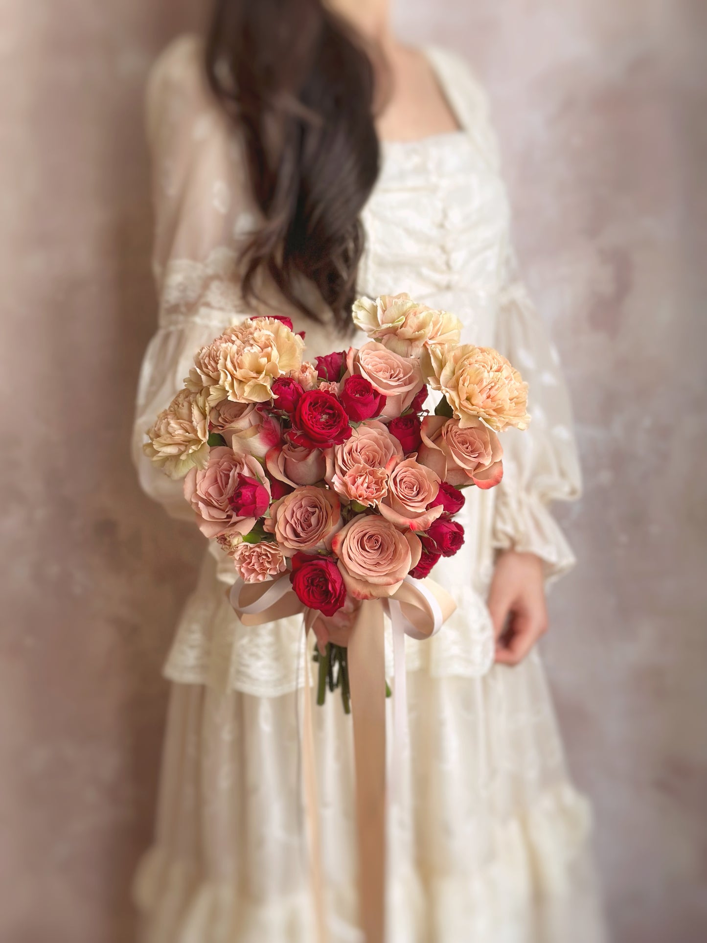 Holding a vintage themed heart shaped fresh flowers cappuccino roses bridal bouquet. The bouquet held in front of a bride’s wedding gown, the heart shape perfectly complementing the romantic bridal look.
新娘手持捧花,搭配婚纱,心形设计与浪漫的新娘造型完美契合。
