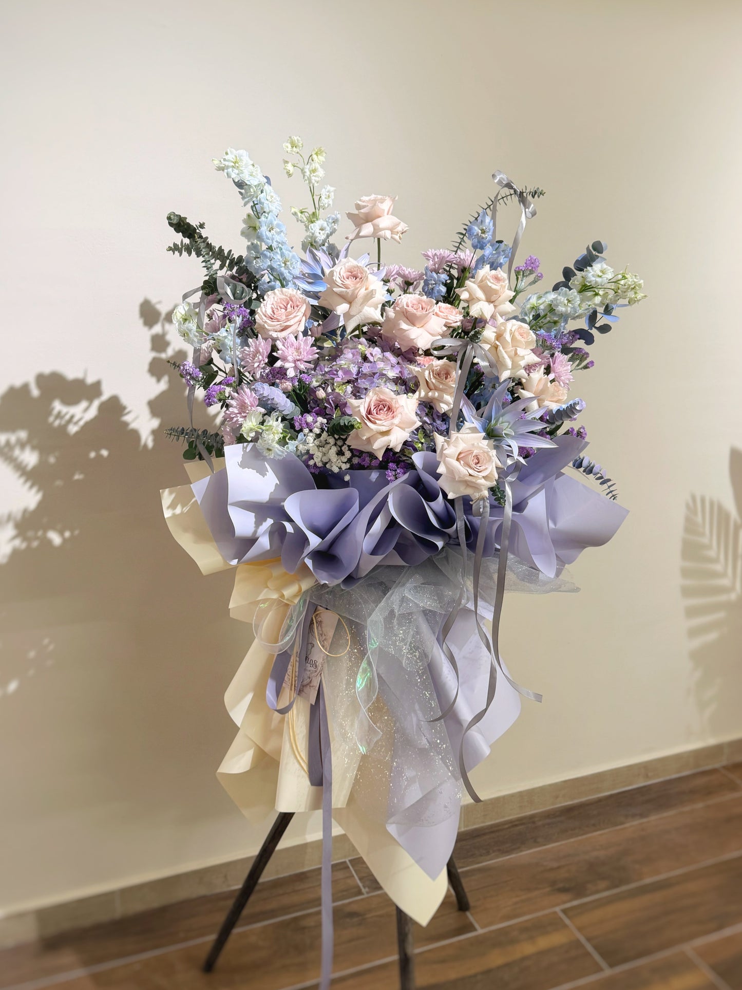 Floral arrangement with pastel colors on a stand against a plain wall.
Front view of a premium fresh flower grand opening stand in soft lilac, pink, and blue hues, featuring pastel ribbons and artistic spray-painted florals.
正面展示高质感开张花篮,融合柔紫、浅粉与清蓝色花材,搭配艺术感喷色与飘逸丝带,营造梦幻氛围。
