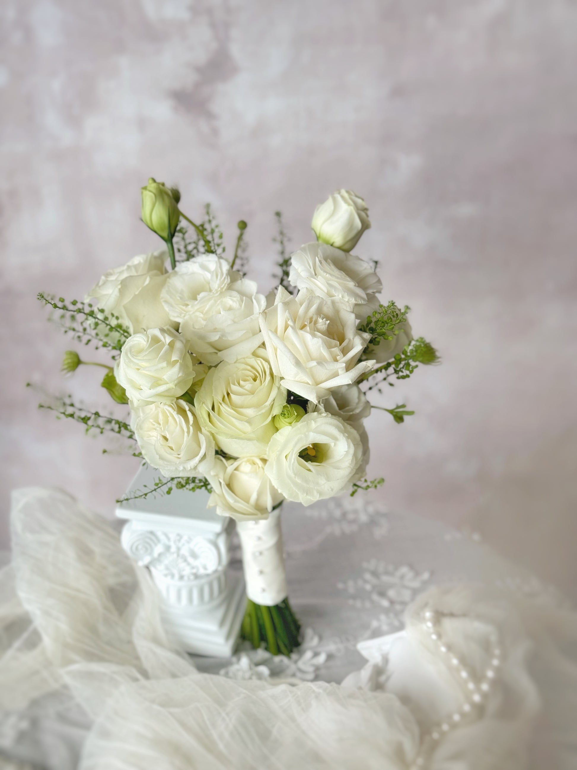 Minimalist white bridal bouquet resting on a table, showcasing the delicate beauty of fresh roses and eustoma flowers.
简约优雅的韩式婚礼捧花,采用白色玫瑰与洋桔梗,散发纯净浪漫气息