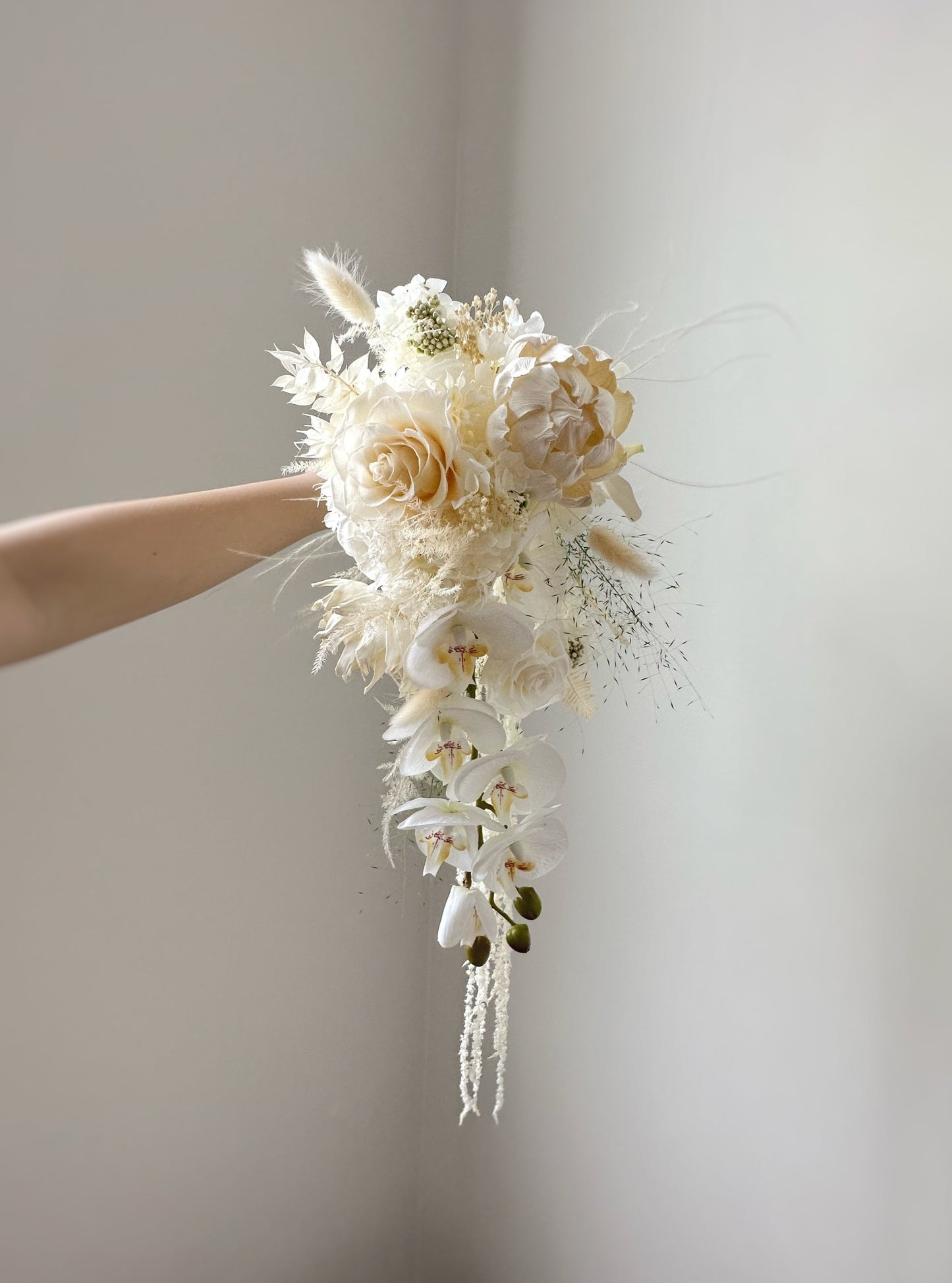Cascading/ teardrop shaped preserved flowers bridal bouquet, creamy white in color, featuring preserved roses, sola flowers and other fillers. A delicate blend of ivory and pastel florals, highlighting intricate textures and soft hues.
象牙白与粉彩花材的细腻搭配,展现精致的花卉质感与柔和色调。