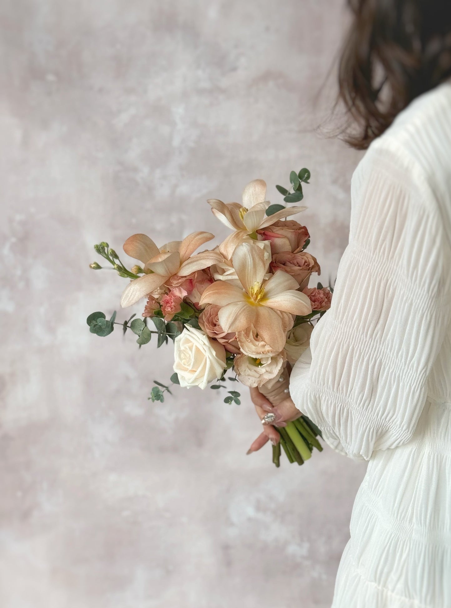 Side view of a model in white dress holding the bridal bouquet, featuring warm cappuccino roses, pastel blooms, and delicate light brown tulips 
低饱和柔和花色,打造梦幻浪漫的新娘捧花,尽显复古优雅