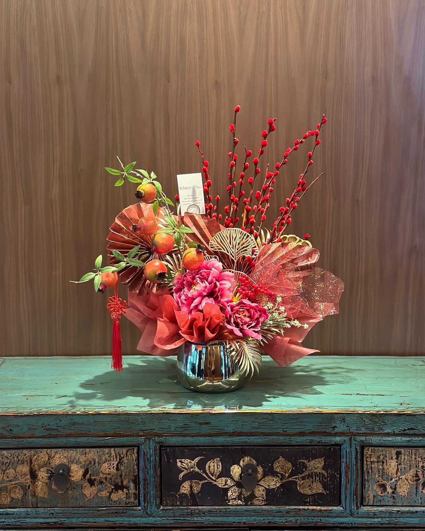 faux peony and pomegranate CNY themed vase arrangement on antique cabinet.
