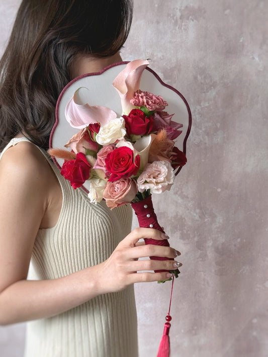 A model holding a chic and modern oriental-style bridal fan bouquet in front of her face, blending tradition with a fresh floral touch, 现代东方风格新娘扇花束,融合传统与现代设计