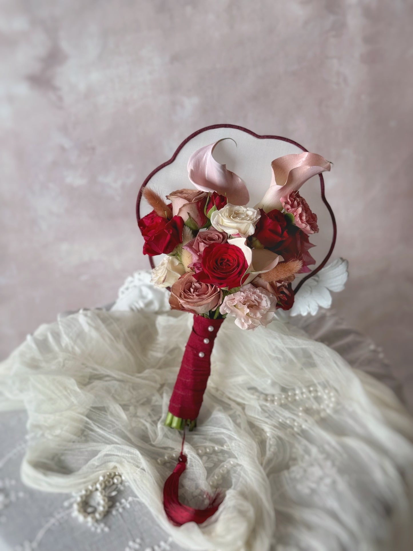 Floral bridal fan bouquet resting on a table, showcasing an artistic blend of fresh blooms on a beautifully crafted Chinese wedding fan. 红色系中式团扇捧花中式婚礼