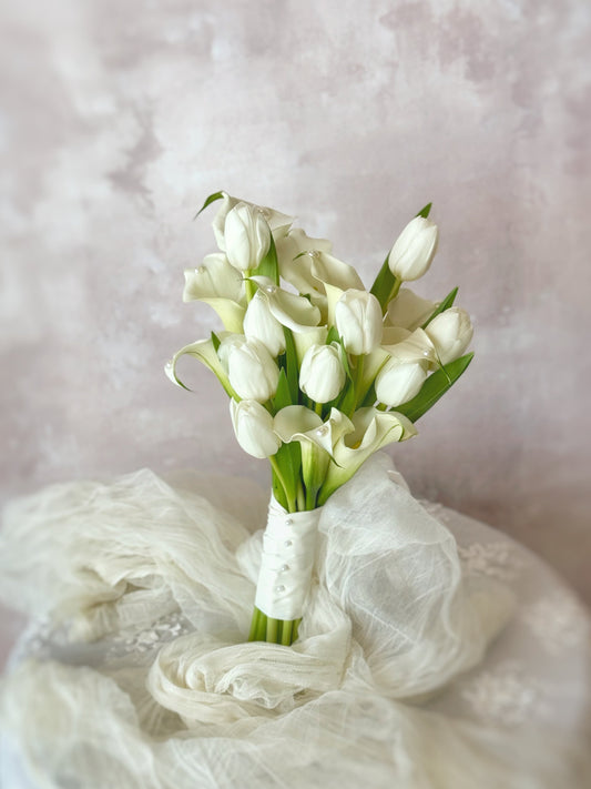 Front view of Genuine fresh flowers bridal bouquet, a minimalist bridal bouquet featuring elegant calla lilies and tulips, arranged on a table for a clean and modern look. 与传统新娘花束不同,这款郁金香与马蹄莲捧花展现极简优雅风格