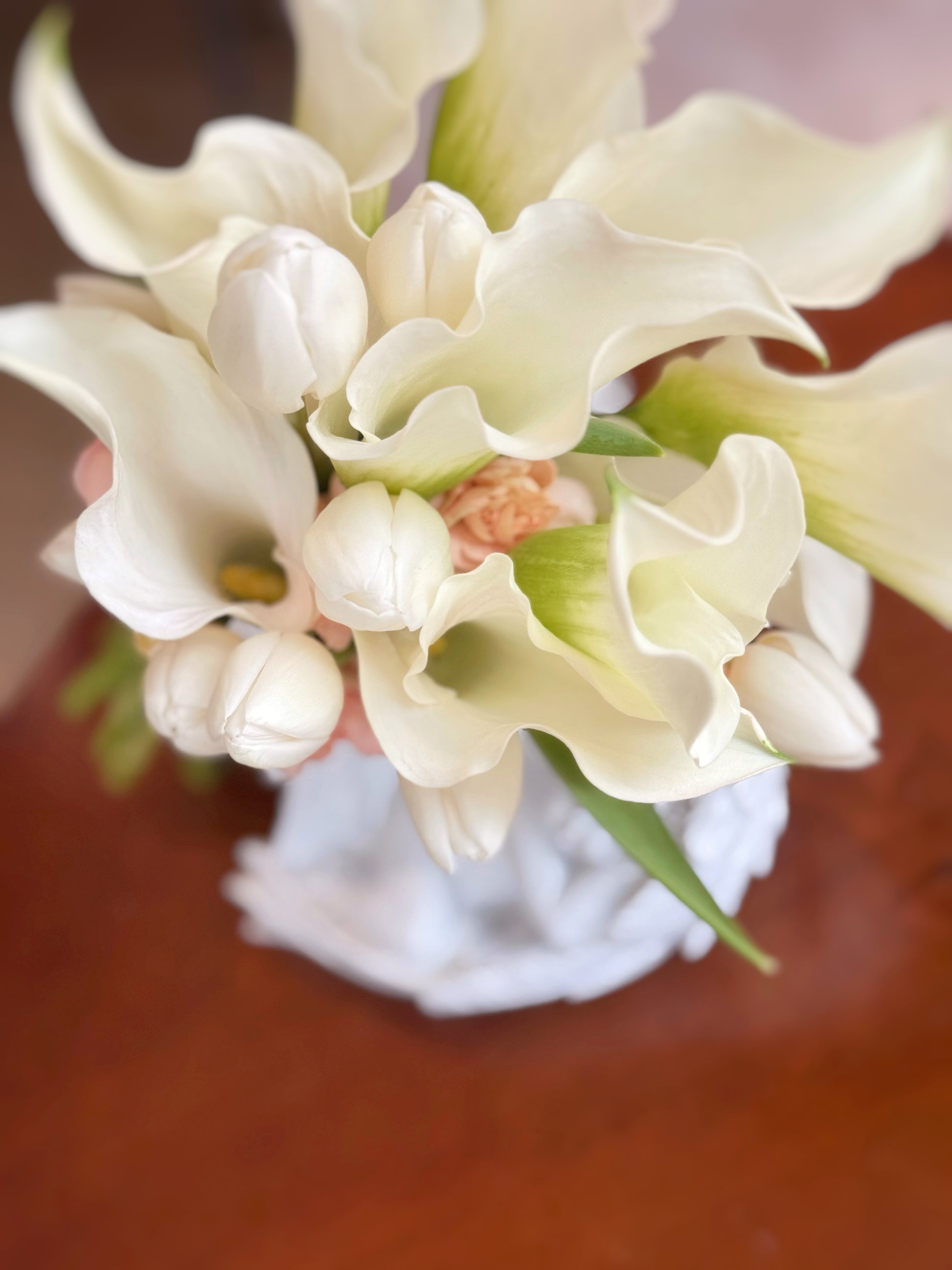 Close-up of elegant calla lilies and delicate tulips accented by peach spray carnations, highlighting smooth petal textures.
马蹄莲与郁金香特写,辅以桃色小康乃馨,细致展现花瓣柔滑质感。