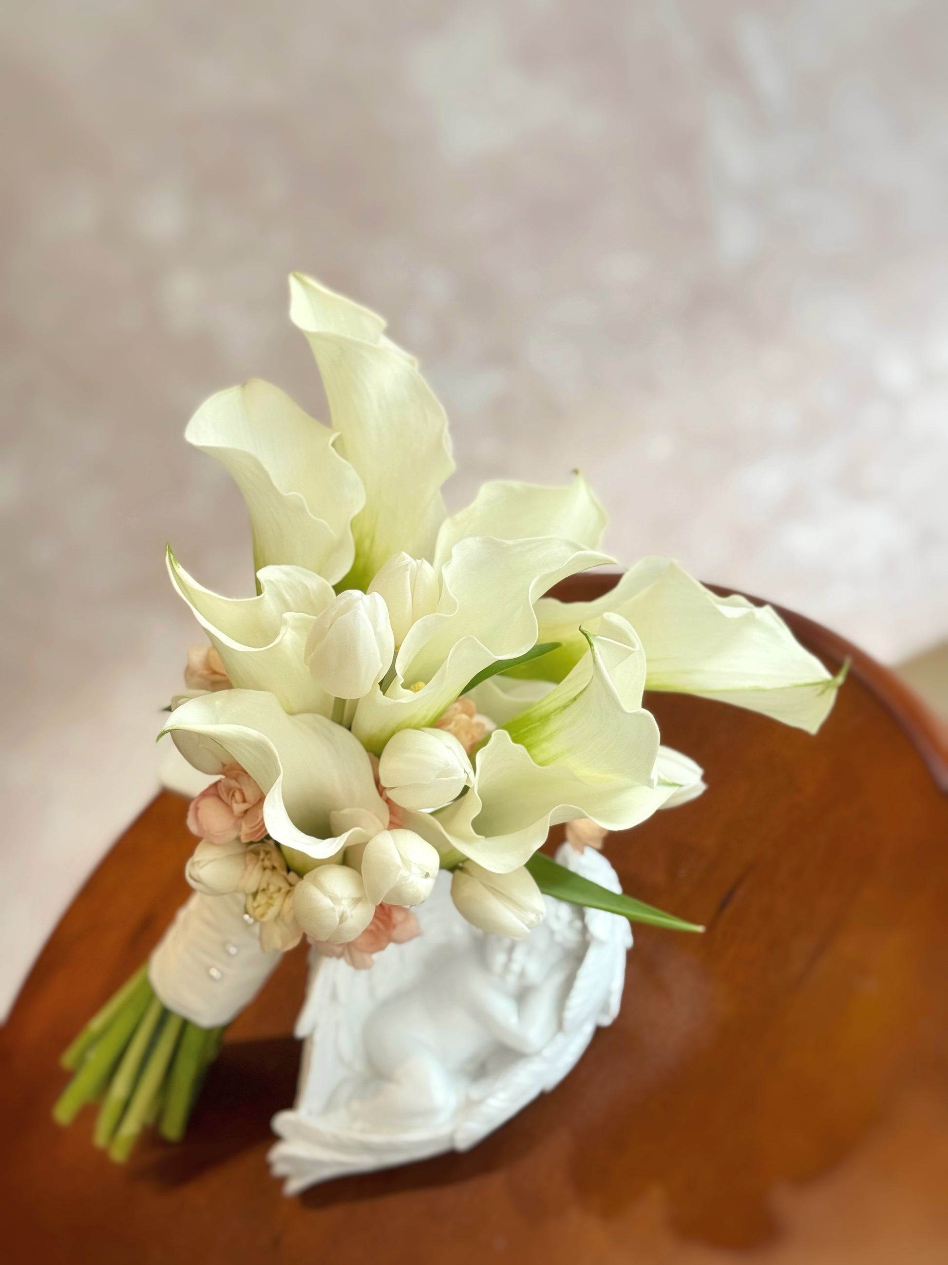 Minimalist calla lilies and tulips bridal bouquet arranged on a table, radiating fresh elegance and understated beauty perfect for a wedding setting.
简约白色马蹄莲郁金香新娘捧花摆放于桌面,散发清新优雅与低调美感,适合婚礼氛围。