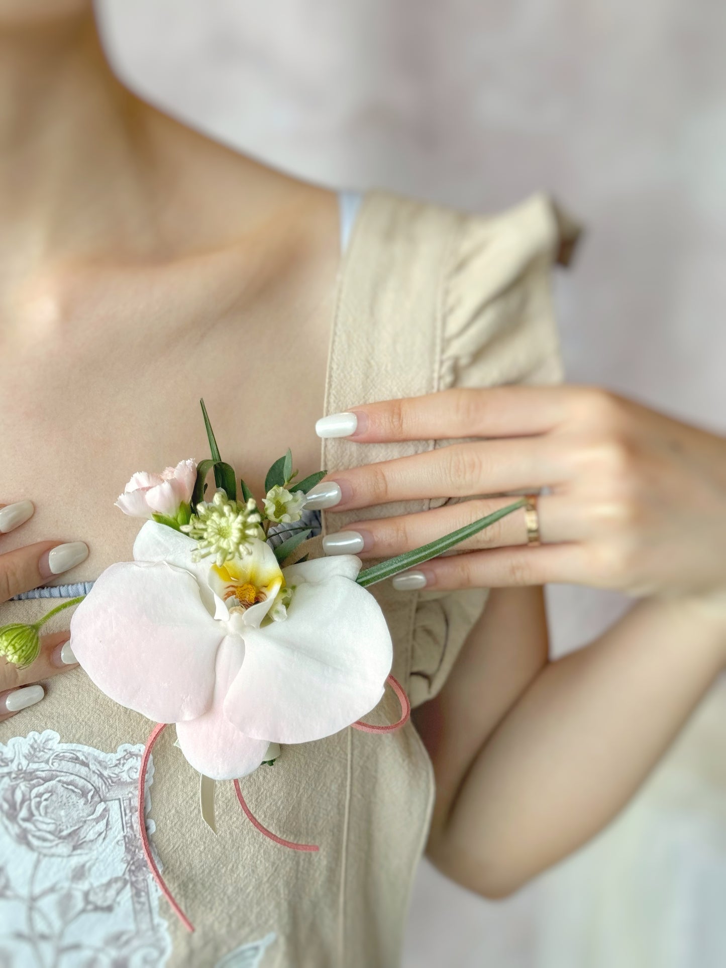 Model wearing a pink-themed Phalaenopsis orchid corsage with seasonal fillers and foliage, exuding elegance and charm