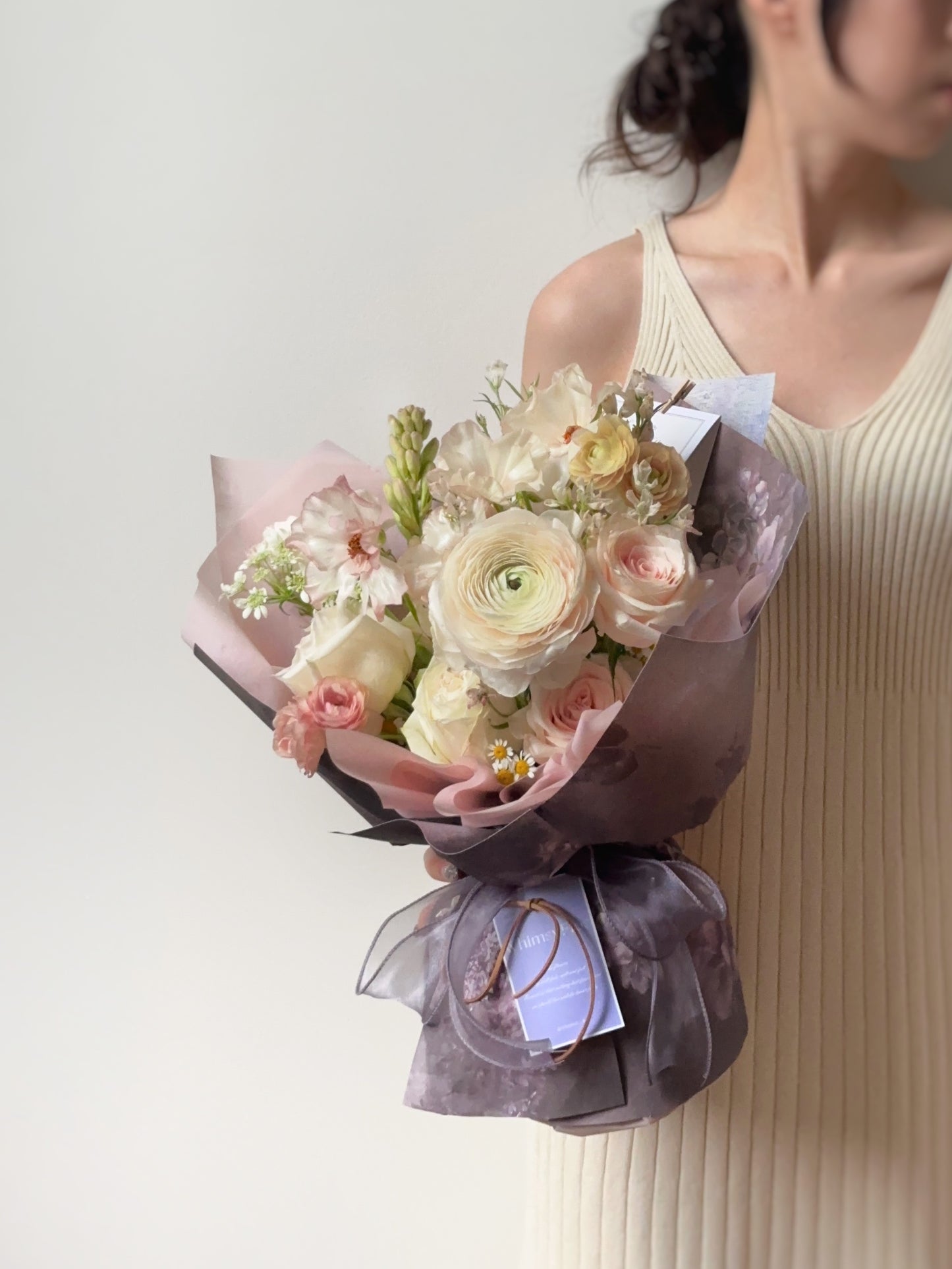 Side angle of the bouquet highlighting the layering of blush and cream blooms against lavender wrapping.
从侧面拍摄,展示花束中粉色与奶油色花朵的层次感,配以薰衣草灰包裹纸。