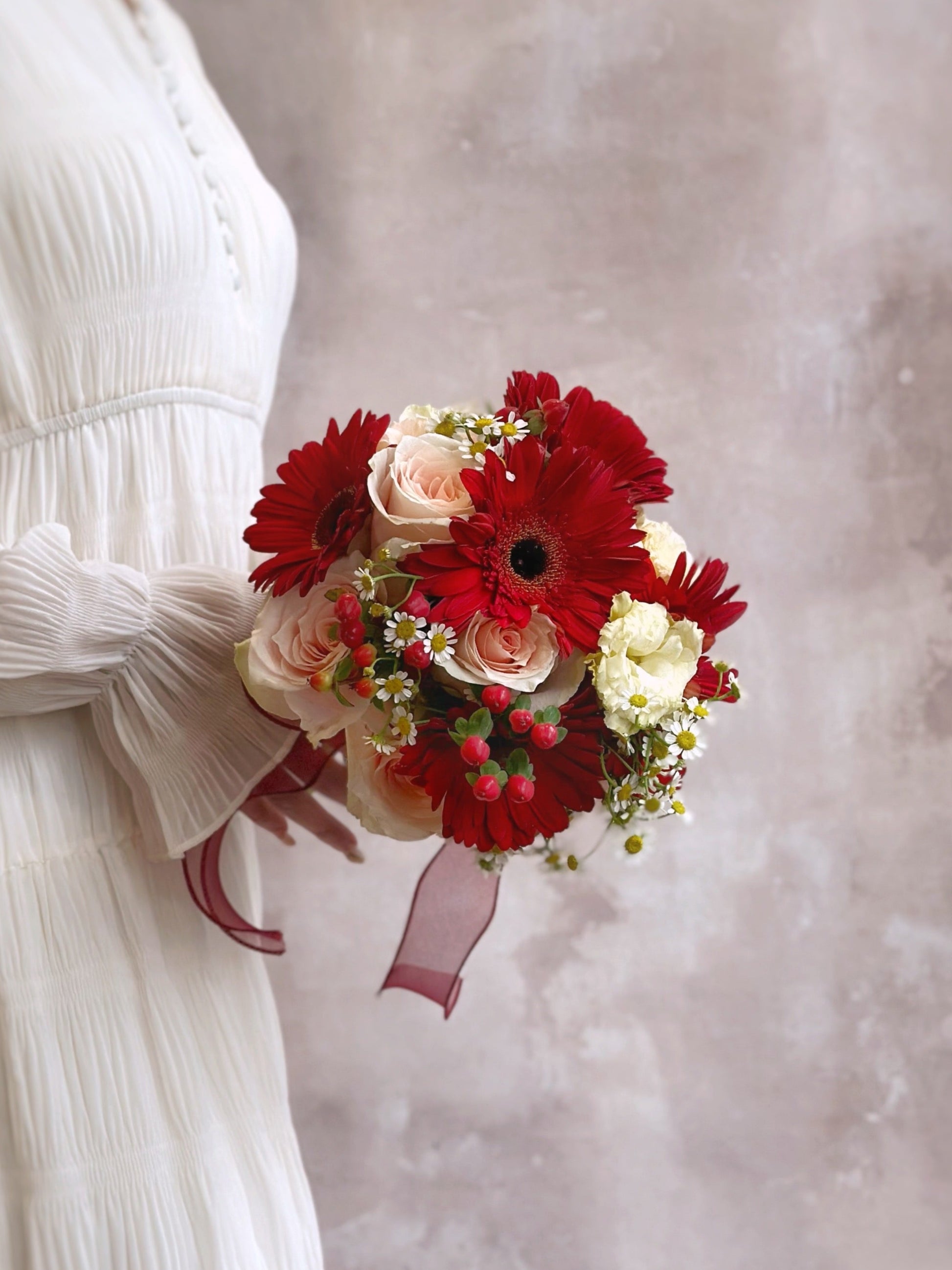A cheerful and distinctive floral round bouquet with a rustic aesthetic, featuring red gerbera, peachy pink rose, chamomile and eustoma
充满田园气息的欢快圆形新娘捧花,展现独特魅力,红色非洲菊, 洋甘菊桃粉色玫瑰 和洋桔梗