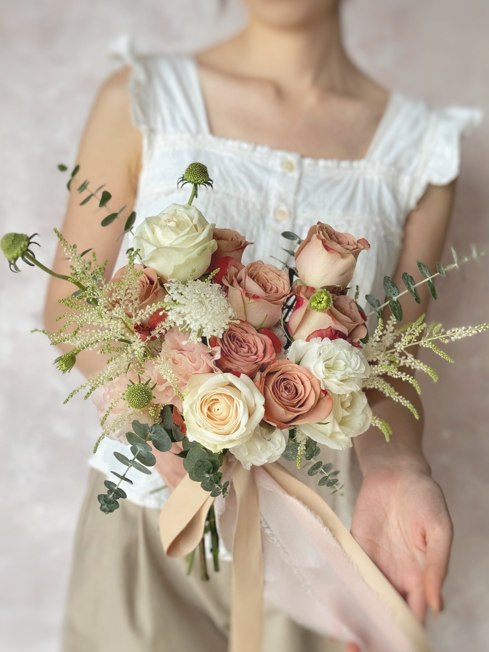 A model holding a beautifully arranged fan-shaped fresh flowers wedding bouquet with cappuccino roses, astilbe, and fresh greenery, perfect for a garden-inspired celebration