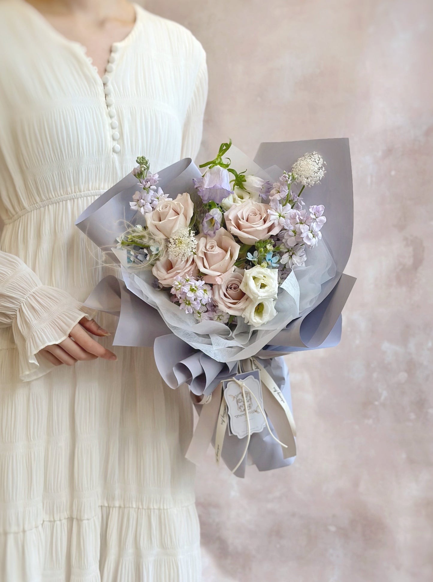 Lilac princess fresh flowers handtied bouquet in luxe size, held by model on front view. Front view of a whimsical lilac and baby blue bouquet with soft cool-toned flowers. 正面展示带有梦幻淡紫与婴儿蓝色调的冷感系花束全貌。