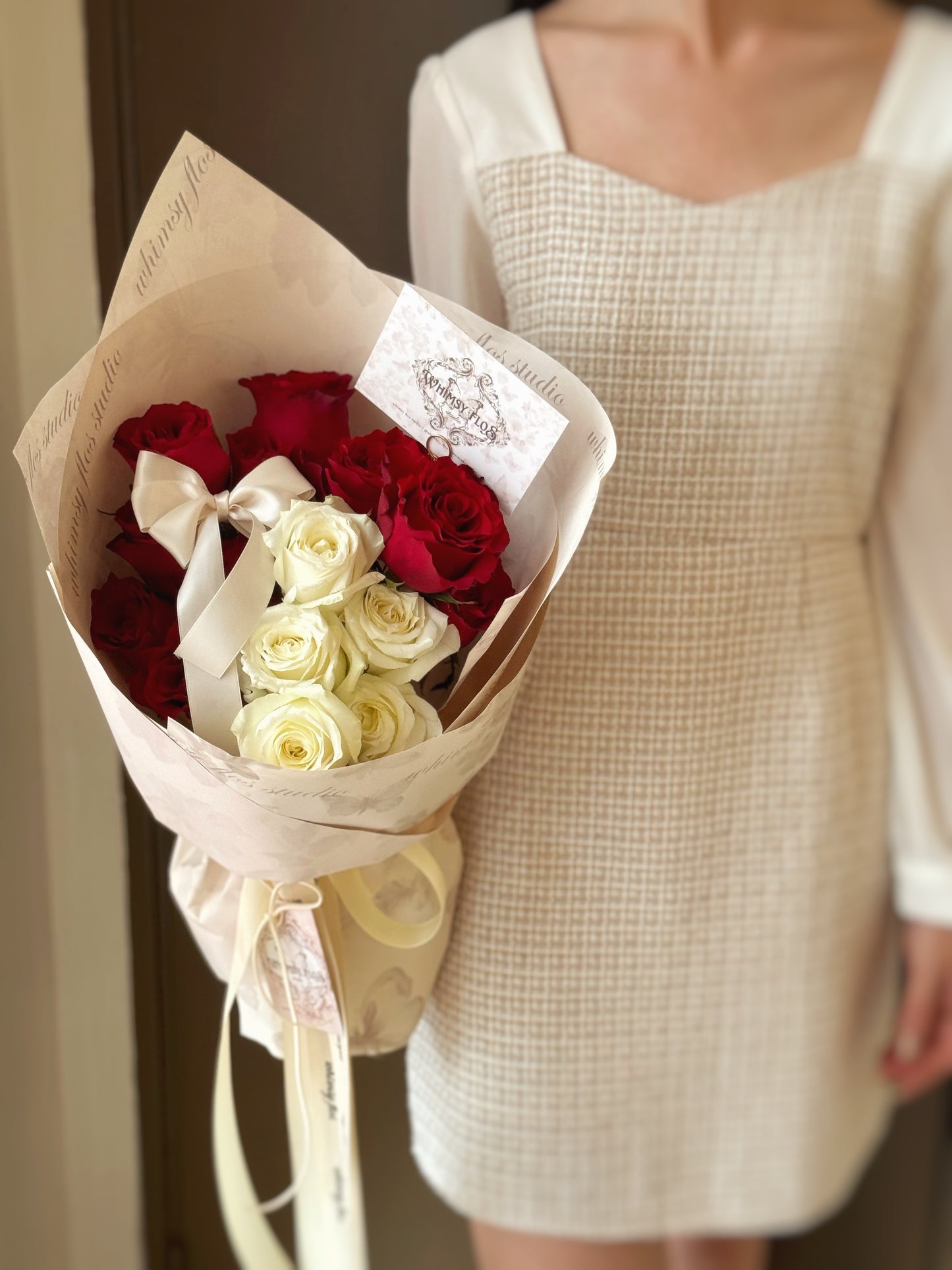 Model holding Luna Kiss bouquet of red and white fresh roses, elegantly wrapped in minimalist style with silky double bow ribbons