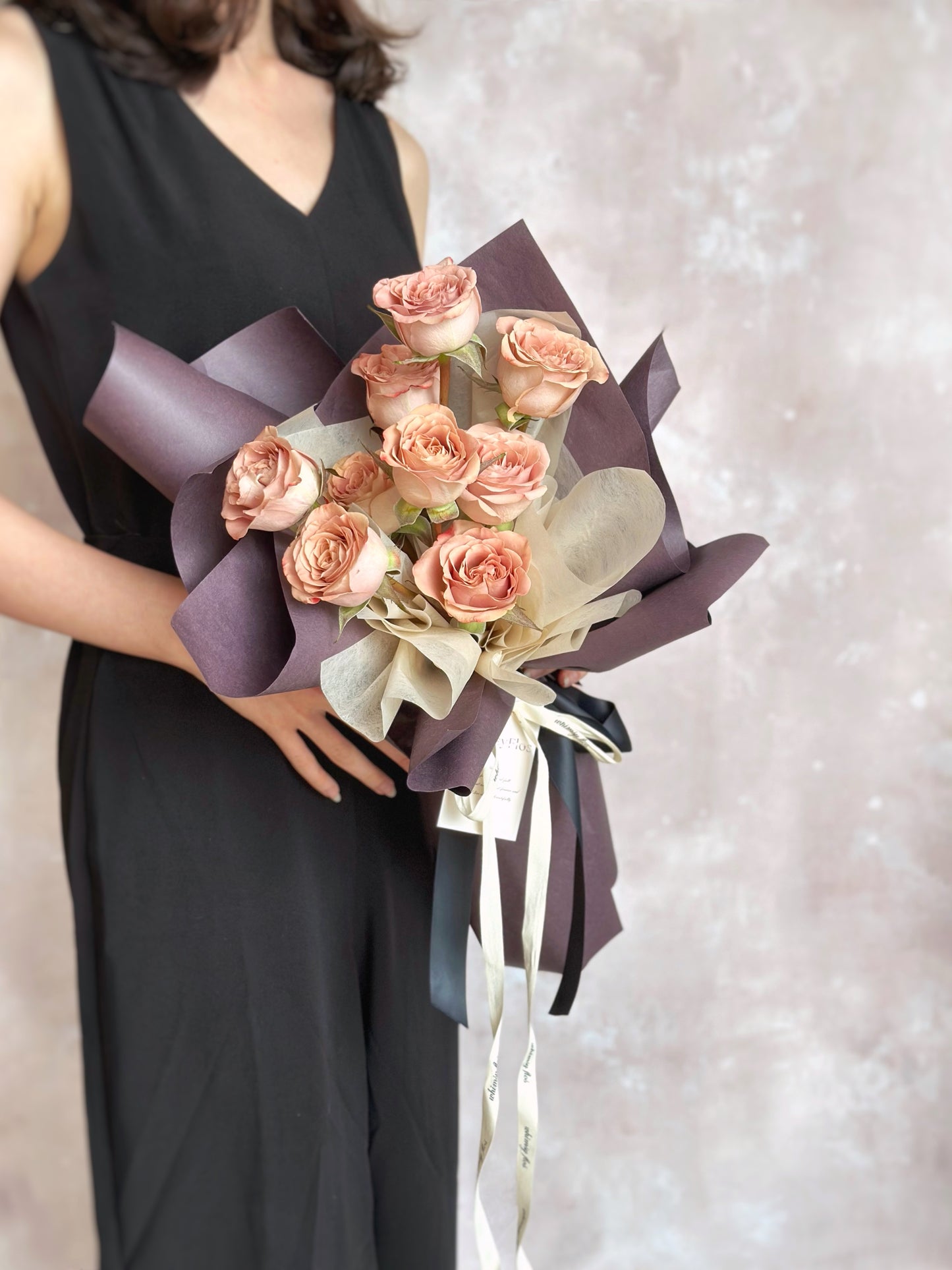 Front view of a romantic bouquet featuring cappuccino roses in dusty pink, wrapped in deep mauve sculptural layers for a soft yet dramatic look.
正面展示复古浪漫花束,焦点为尘粉色卡布奇诺玫瑰,搭配深紫包裹,整体呈现柔和却带有神秘气质的风格。