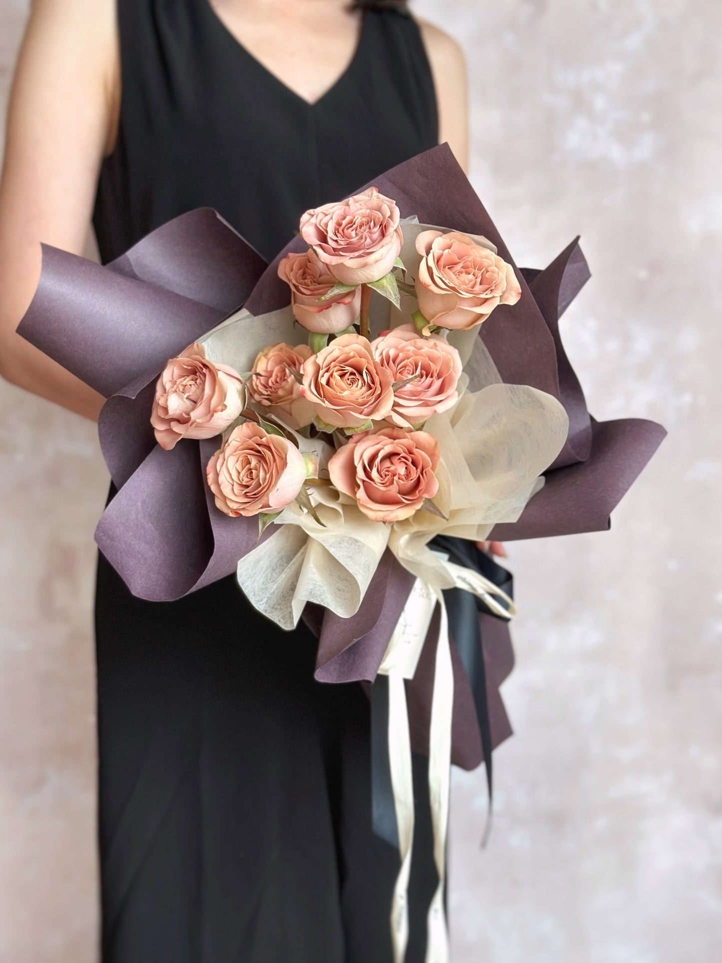 Front view of a romantic bouquet featuring cappuccino roses in dusty pink, wrapped in deep mauve sculptural layers for a soft yet dramatic look.
正面展示复古浪漫花束,焦点为尘粉色卡布奇诺玫瑰,搭配深紫包裹,整体呈现柔和却带有神秘气质的风格。