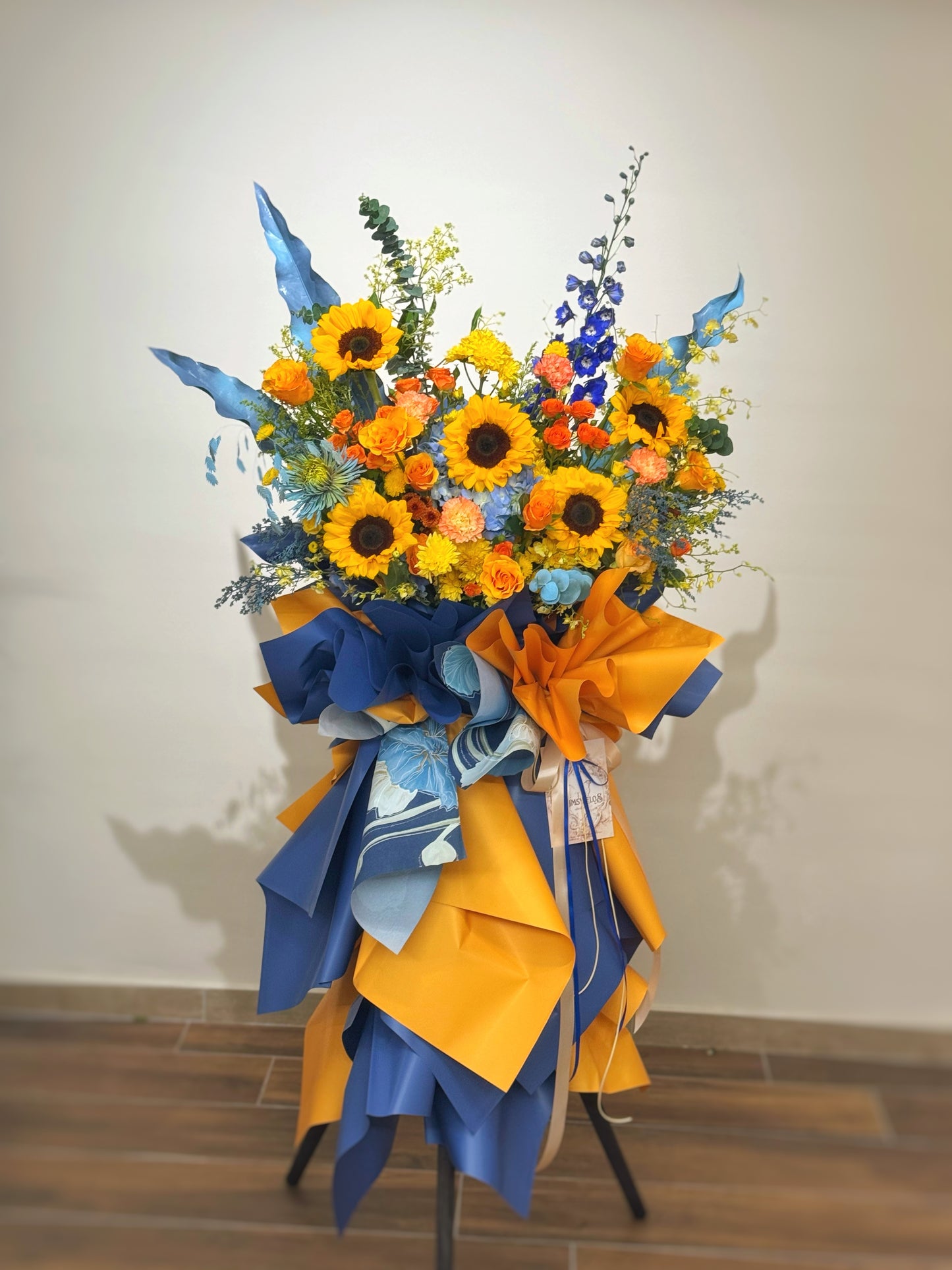 Grand opening flowers with blue and yellow ribbons on a stand against a plain background