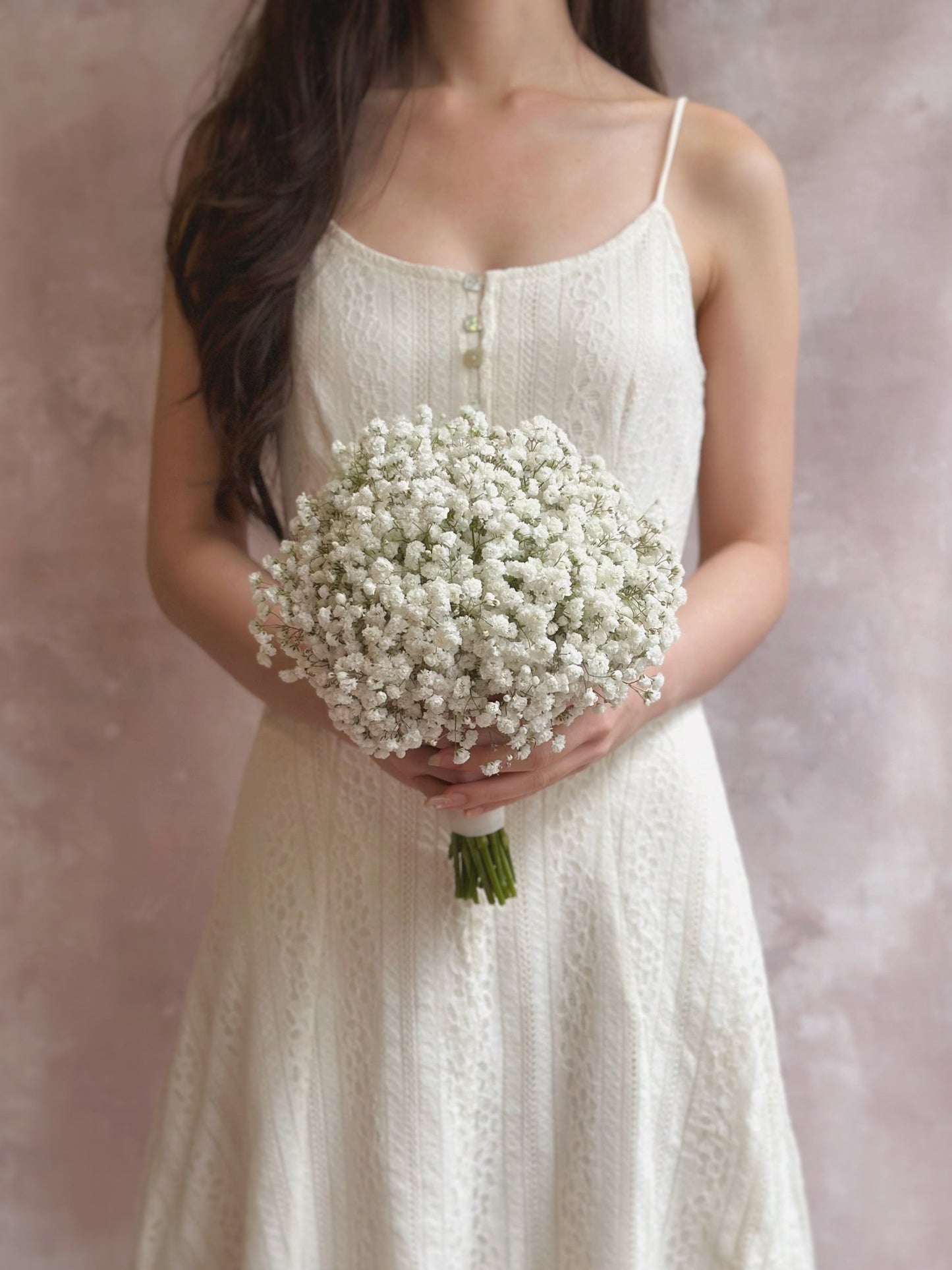 Bride holding a round bouquet of white baby’s breath in front of her, timeless and elegant
新娘手持圆形满天星捧花,经典优雅