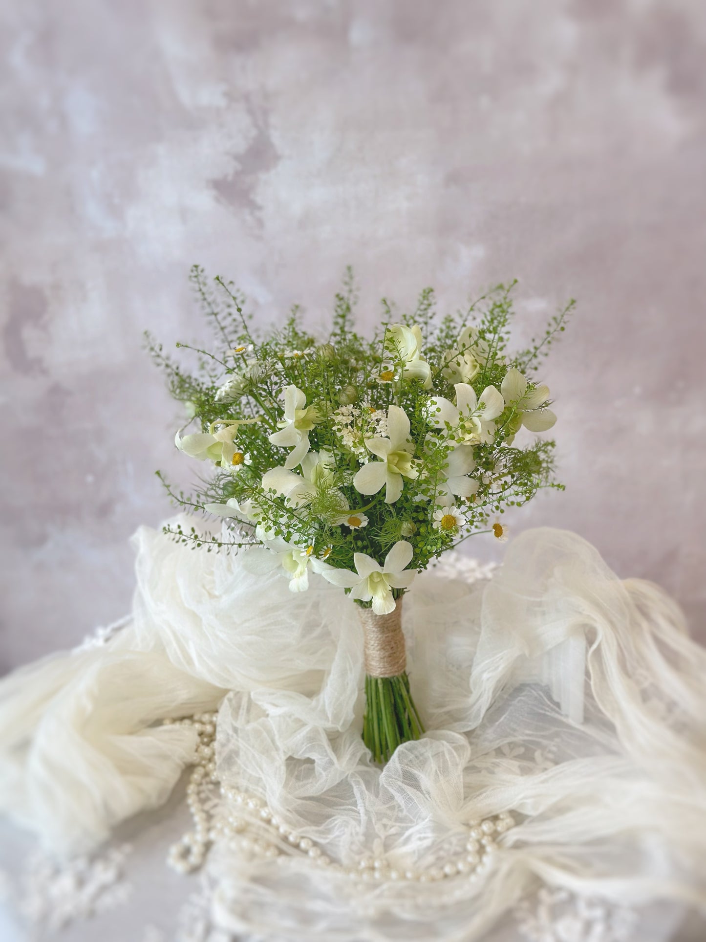 Misty forest fresh flowers bridal bouquet front view. A delicate hand-tied bouquet of ivory wildflowers and organic greenery rests beautifully on a soft linen tablecloth, evoking a dreamy garden wedding vibe.
 手工绑扎的象牙色野花捧花搭配绿叶,静静地摆放在柔软的麻布桌布上,散发出梦幻花园婚礼的气息。
