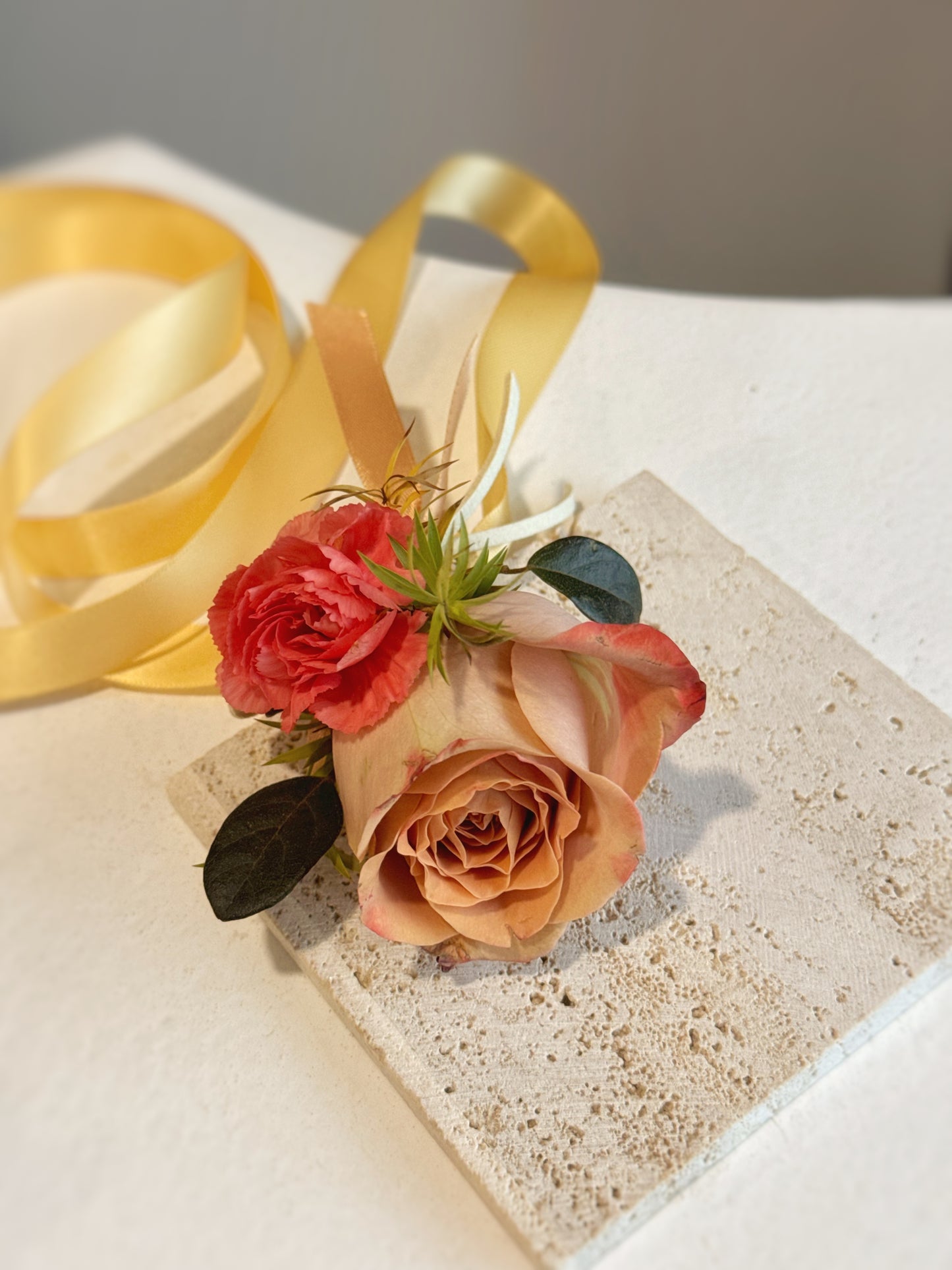 The Mocha Sunset wrist corsage placed on a block, highlighting its nude pink cappuccino rose and rich fall-toned accents.