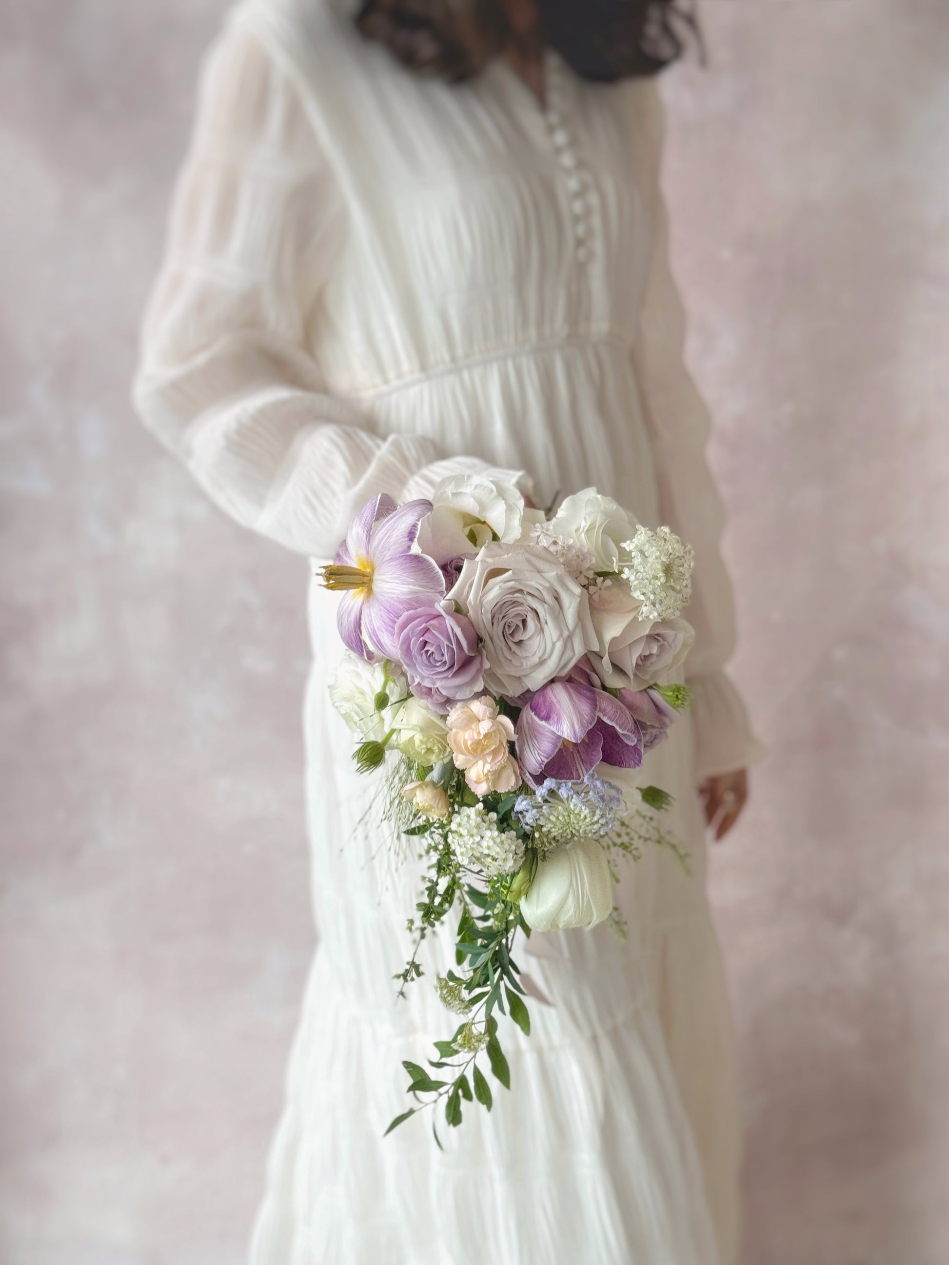 A model in white dress holding Ocean eyes bouquet, a cascading Phalaenopsis orchid bouquet in lilac and white, creating an elegant and timeless bridal look
新娘手持 Ocean Eyes 捧花,蝴蝶兰垂坠营造空灵唯美感; 紫丁香与白色泪滴型捧花,优雅衬托新娘造型