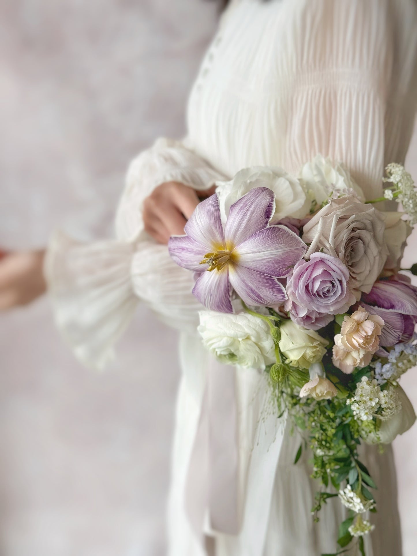 Side closed up view of Ocean eyes teardrop bridal bouquet held by a model, showing elegant floral details, with violet tulips, soft lilac and white orchids creating a natural, flowing silhouette