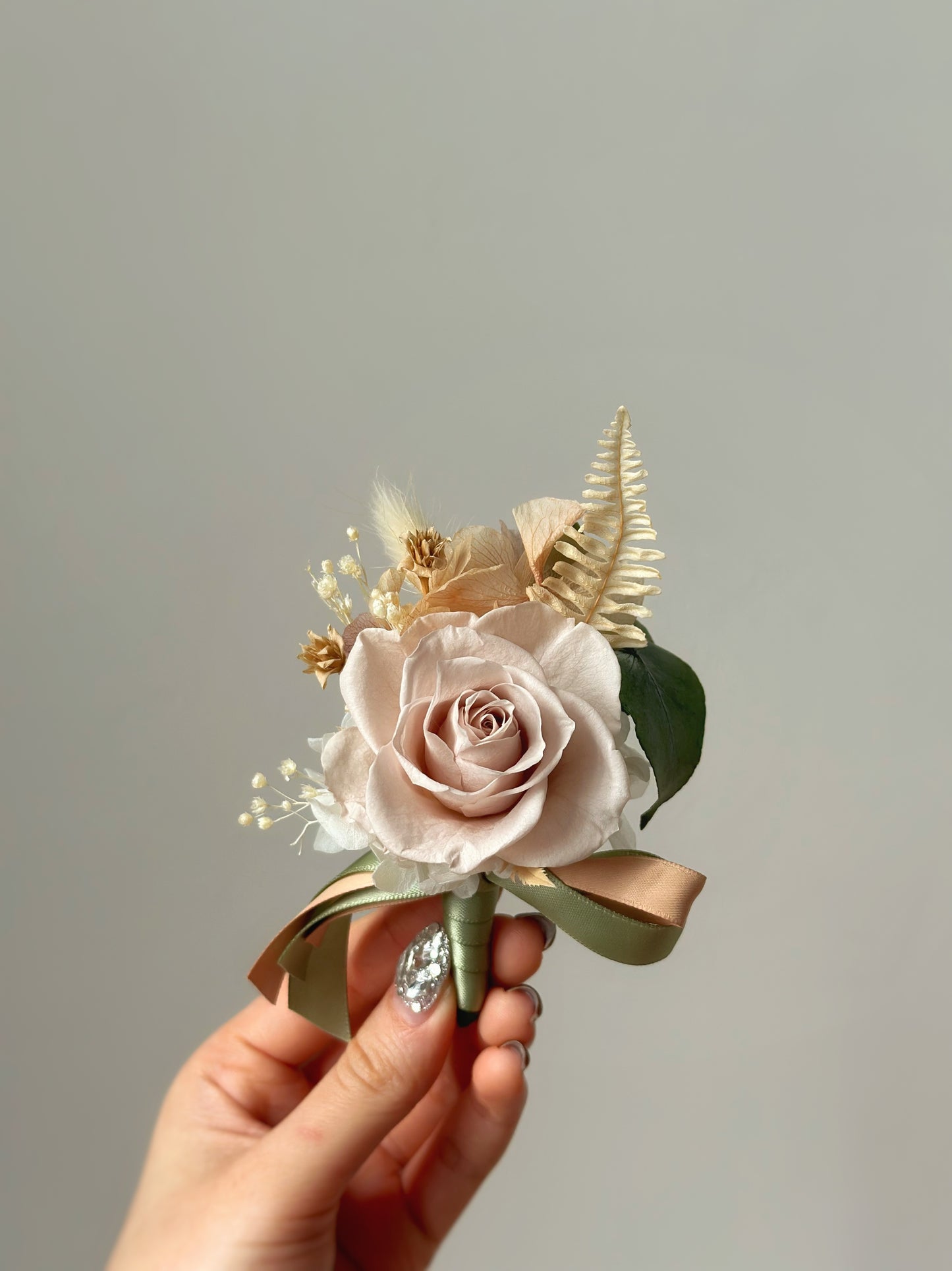 olive preserved rose boutonniere holding by model