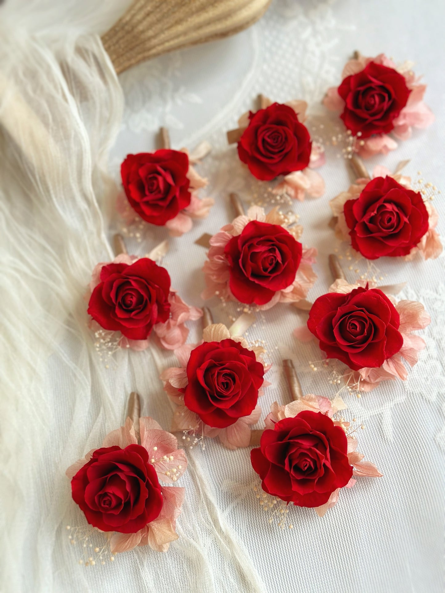 Multiple red boutonnieres arranged on a table in a zoomed-out view, showcasing their oriental-inspired design and rich floral details