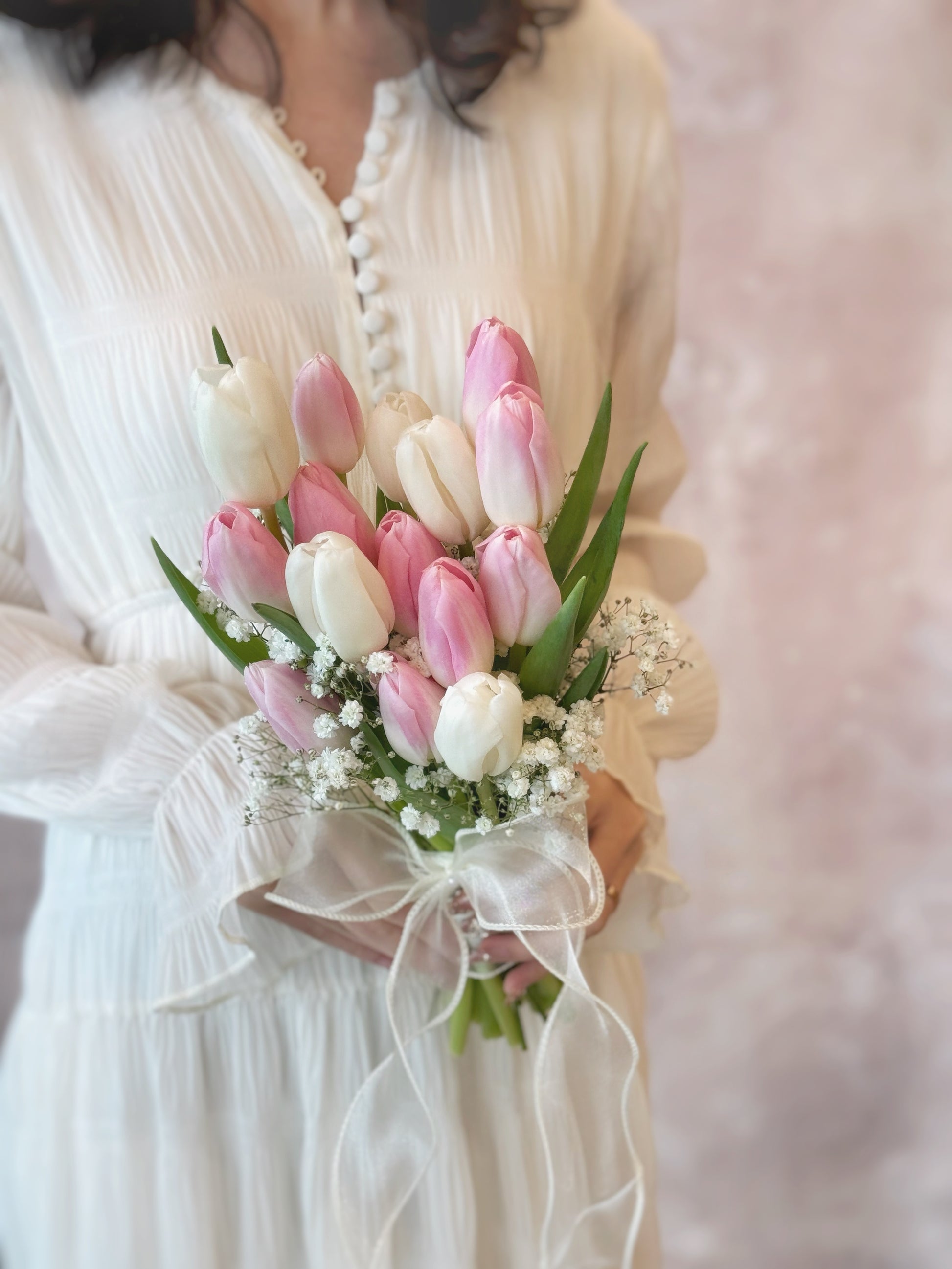 A bride holding a romantic Korean-inspired bouquet with pink and white tulips, surrounded by baby’s breath
新娘手持韩式粉白郁金香捧花,搭配满天星,温柔浪漫