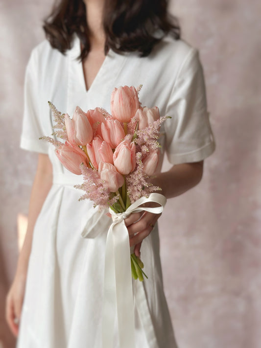 A bride holding a minimalist bouquet of peachy pink tulips and airy astilbe, exuding soft elegance
新娘手持极简风捧花,桃粉郁金香与泡泡草展现温柔优雅
