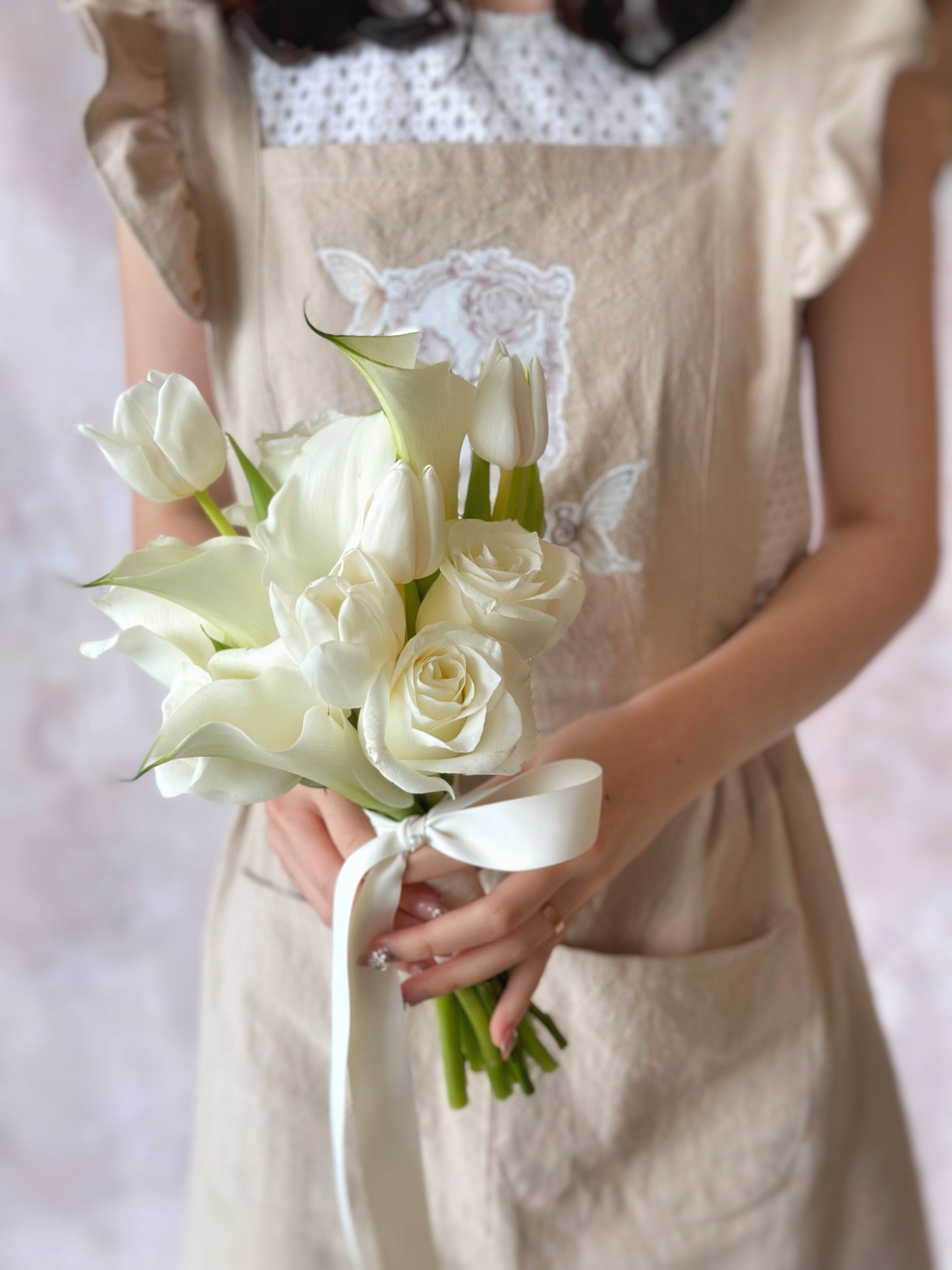 A bride holding a minimalist all-white bouquet of calla lilies, tulips, and roses for a sleek, elegant look
新娘手持极简风白色捧花,马蹄莲、郁金香与玫瑰展现简约优雅