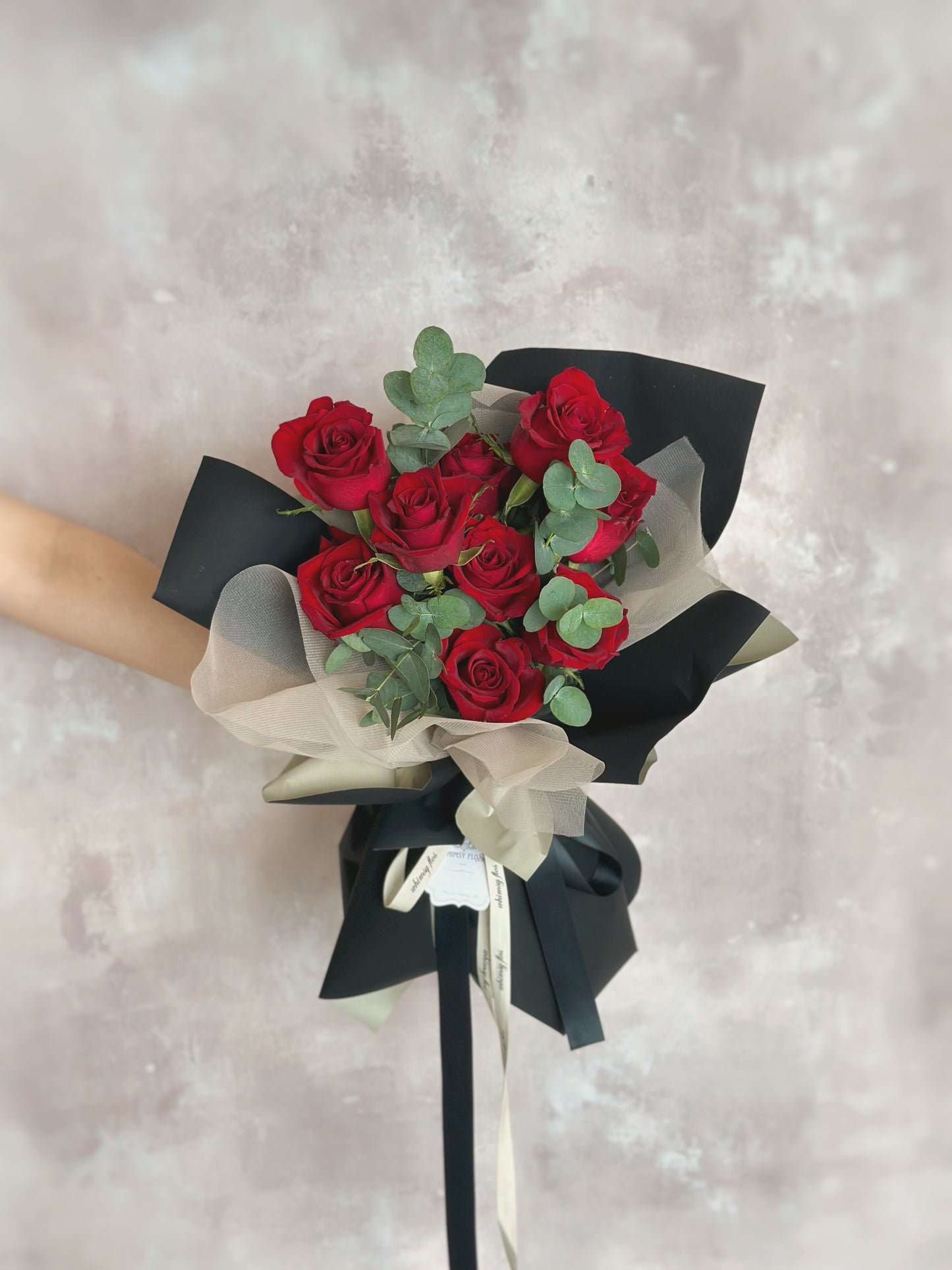 Front view of a modern bouquet with bold red roses and eucalyptus foliage, wrapped in layered black, khaki, and sheer wrapping for contrast and elegance.
正面展示现代感手绑花束,红玫瑰与尤加利叶搭配,采用黑色、卡其与透明包裹,层次分明,气质优雅