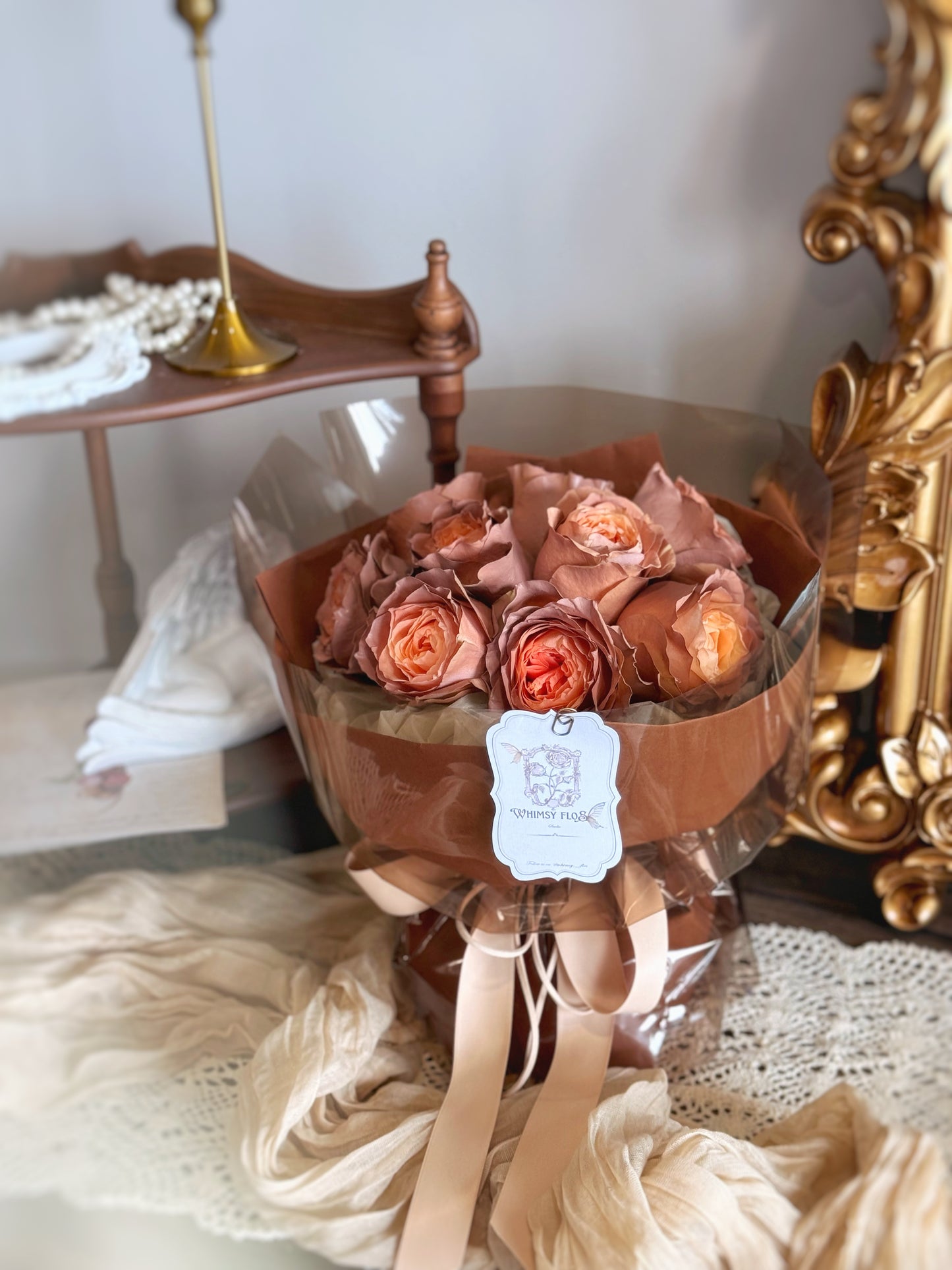 Rose mocha fresh flowers handtied bouquet spray painted rose bouquet in luxe size displayed on table, showing the front view of the bouquet design. 正面展示圆形花束,主花为粉咖玫瑰,花瓣边缘喷涂柔棕色,搭配深棕纸层与透明外包,复古又优雅。