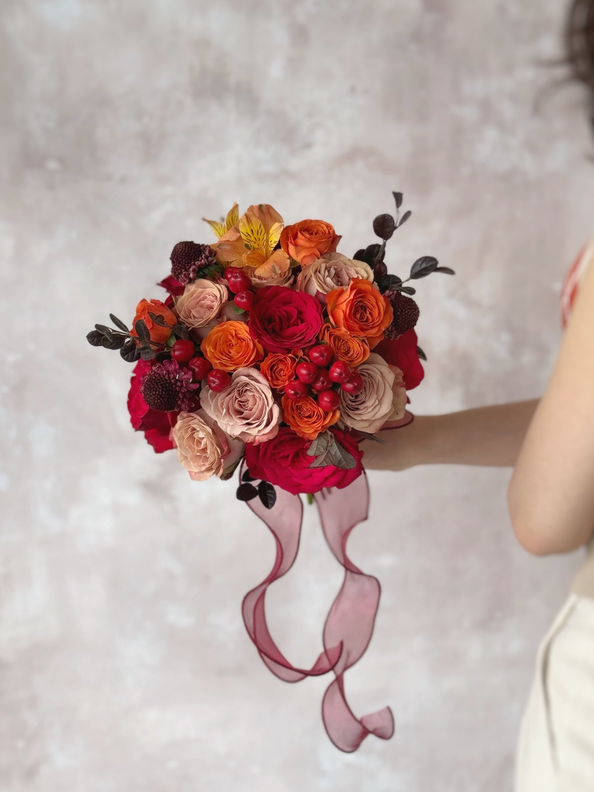 Model holding a bright and bold round bridal bouquet of fresh orange and red roses, inspired by the beauty of a sunset
新娘手持夕阳色调捧花,散发温暖、热情与浪漫气息