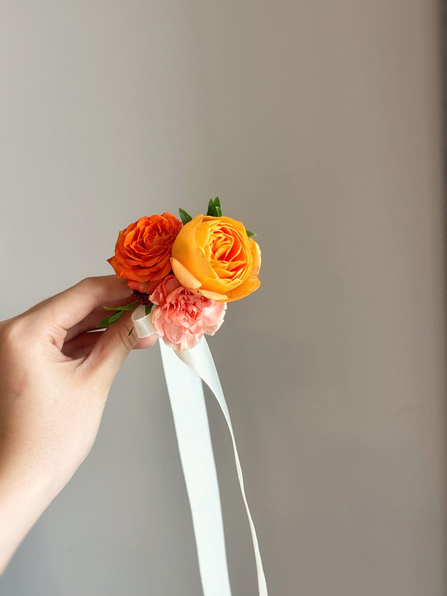 hand holding the Sienna Glow wrist corsage, with soft natural lighting emphasizing the delicate petals and foliage