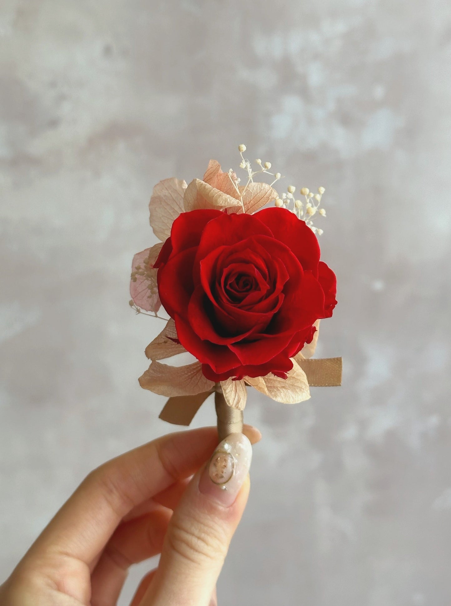 Holding a poppy red rose preserved corsage, close up view