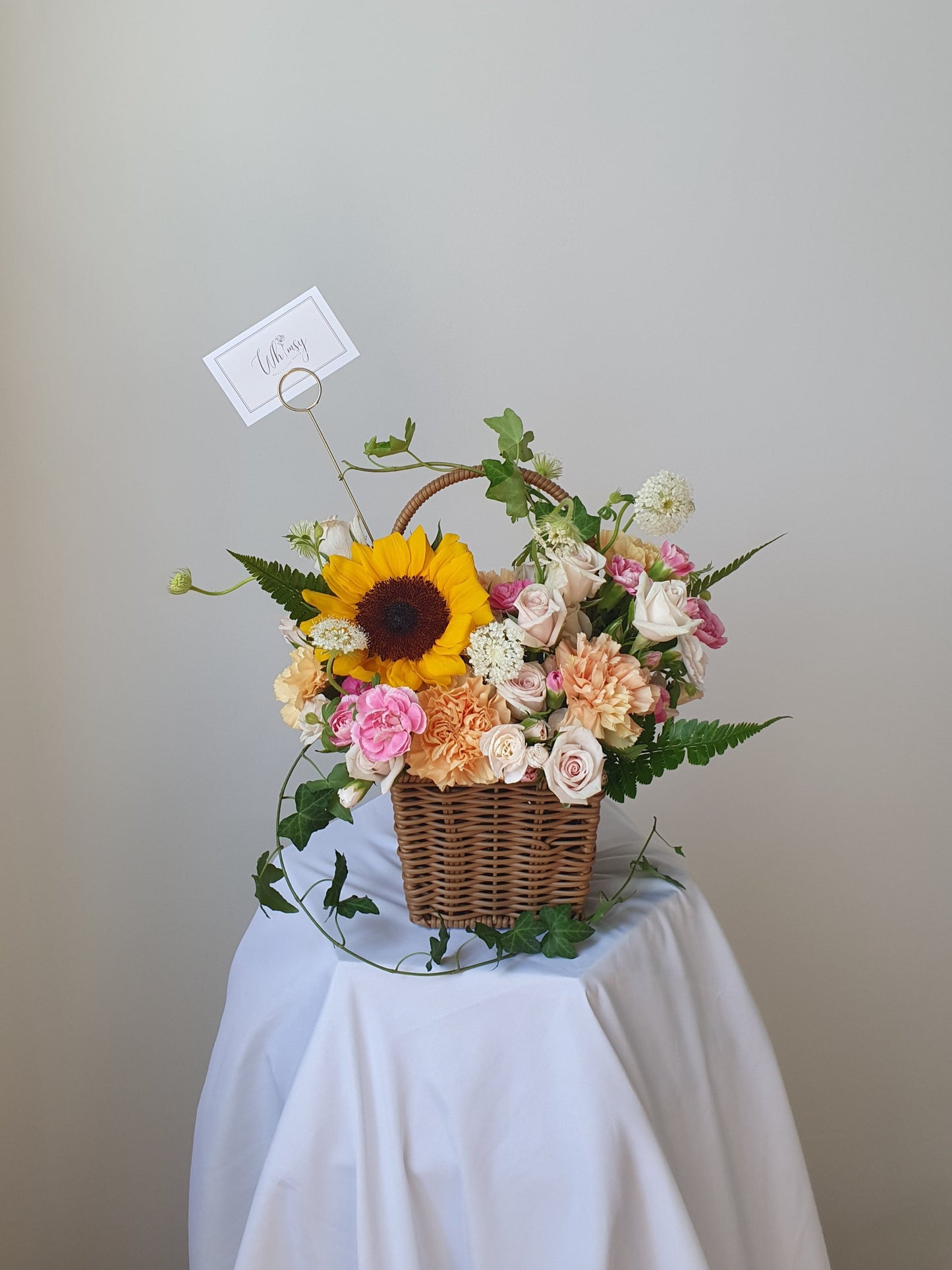 Front view of a cheerful basket arrangement with sunflowers, orange and pink seasonal flowers, and fresh green foliage — bursting with summer energy.
正面展示充满夏日活力的花篮,搭配向日葵、橙粉色花朵与鲜绿叶材,洋溢快乐氛围。