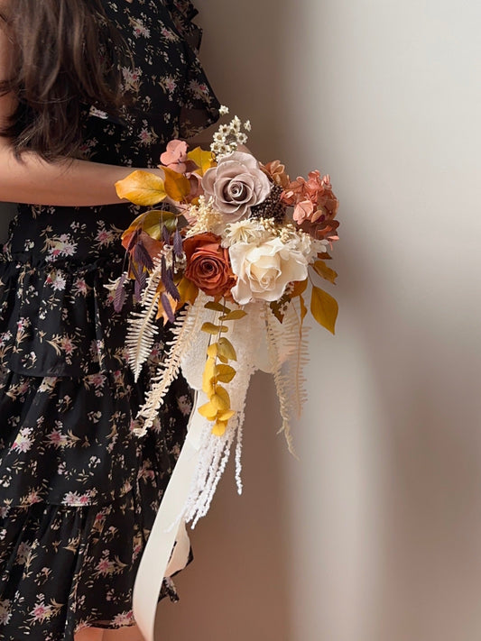 A bride holding the cascading bouquet, adding a touch of bohemian autumn charm to her bridal look.
新娘手持瀑布型捧花,为婚礼造型增添一丝波西米亚秋季浪漫感。