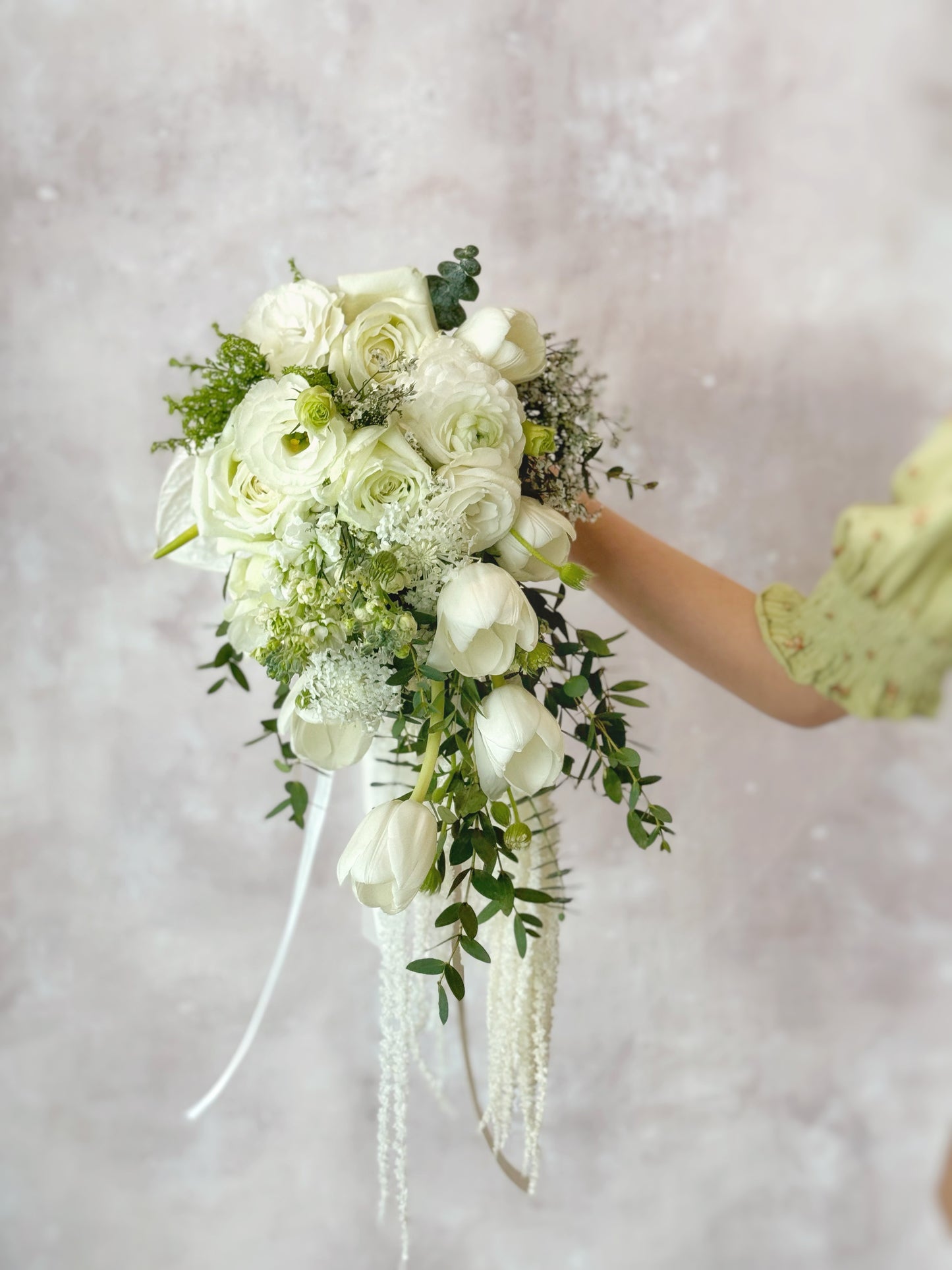 A close-up of the cascading white tulips and wispy greenery, showing the intricate details of this teardrop bridal bouquet. The delicate contrast between the soft, airy flowers and the natural, trailing vines enhances the bouquet’s romantic and timeless appeal.
近距离欣赏垂坠白色郁金香与轻盈绿植的精致细节,这款水滴形新娘捧花通过柔和的花材和自然垂落的藤蔓,呈现出浪漫而经典的婚礼氛围。