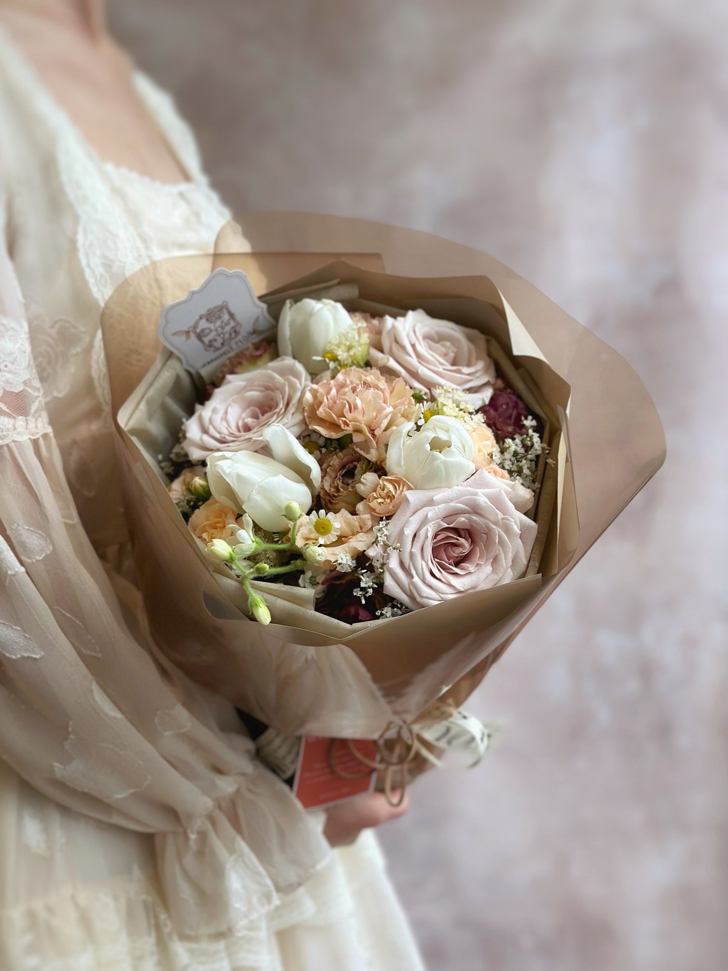 Side angle of the bouquet showing its rounded shape and layered Russian wrapping in muted neutral tones, capturing the vintage-modern blend.
侧面视角展现圆形花束造型与分层俄式包裹设计,低饱和中性色调交织出复古与现代的融合。