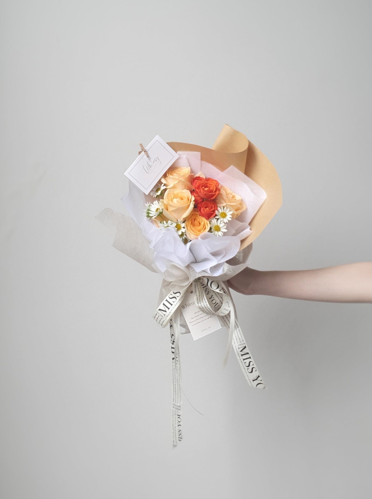 Holding a fresh flowers bouquet featuring  champagne roses, orange spray roses and chamomile 