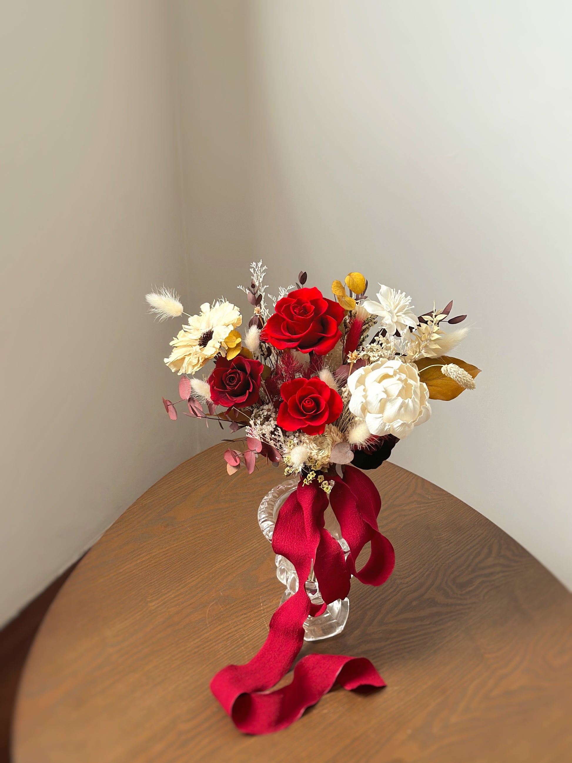 A fan-shaped preserved bridal bouquet inspired by autumn, featuring deep red and mustard yellow blooms.
灵感来自秋季的扇形永生花新娘捧花，搭配深红色和芥末黄花朵。