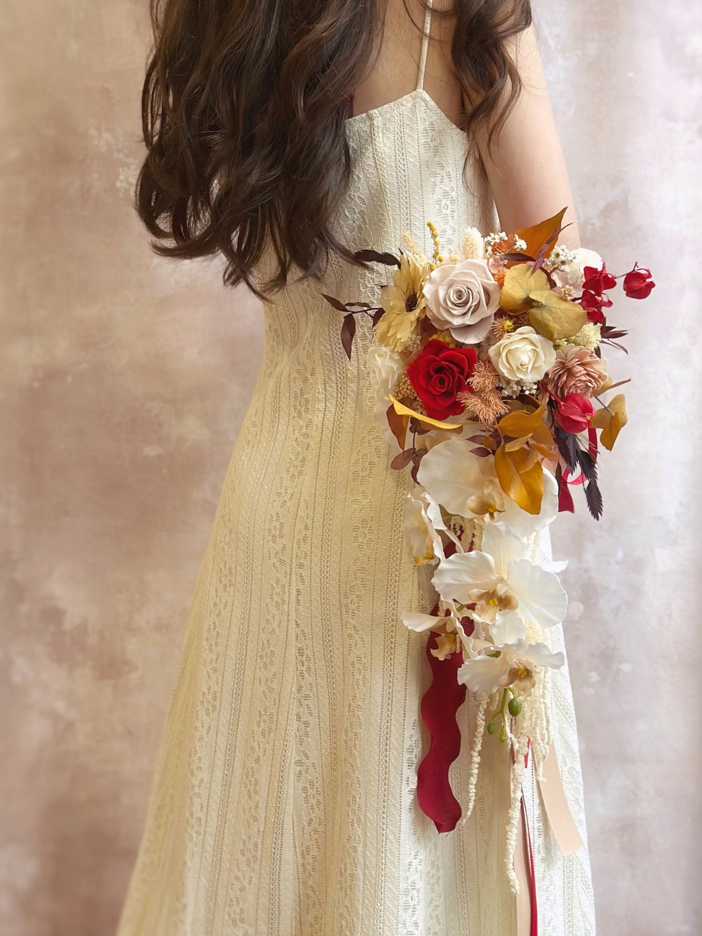 Autumn Whispers cascading preserved flowers bridal bouquet for an autumnal theme wedding ceremony. A bride holding the autumnal teardrop bouquet, its cascading florals and ribbons adding an ethereal, flowing effect.
新娘手持秋日泪滴型捧花，垂坠花材与丝带增添飘逸梦幻感。