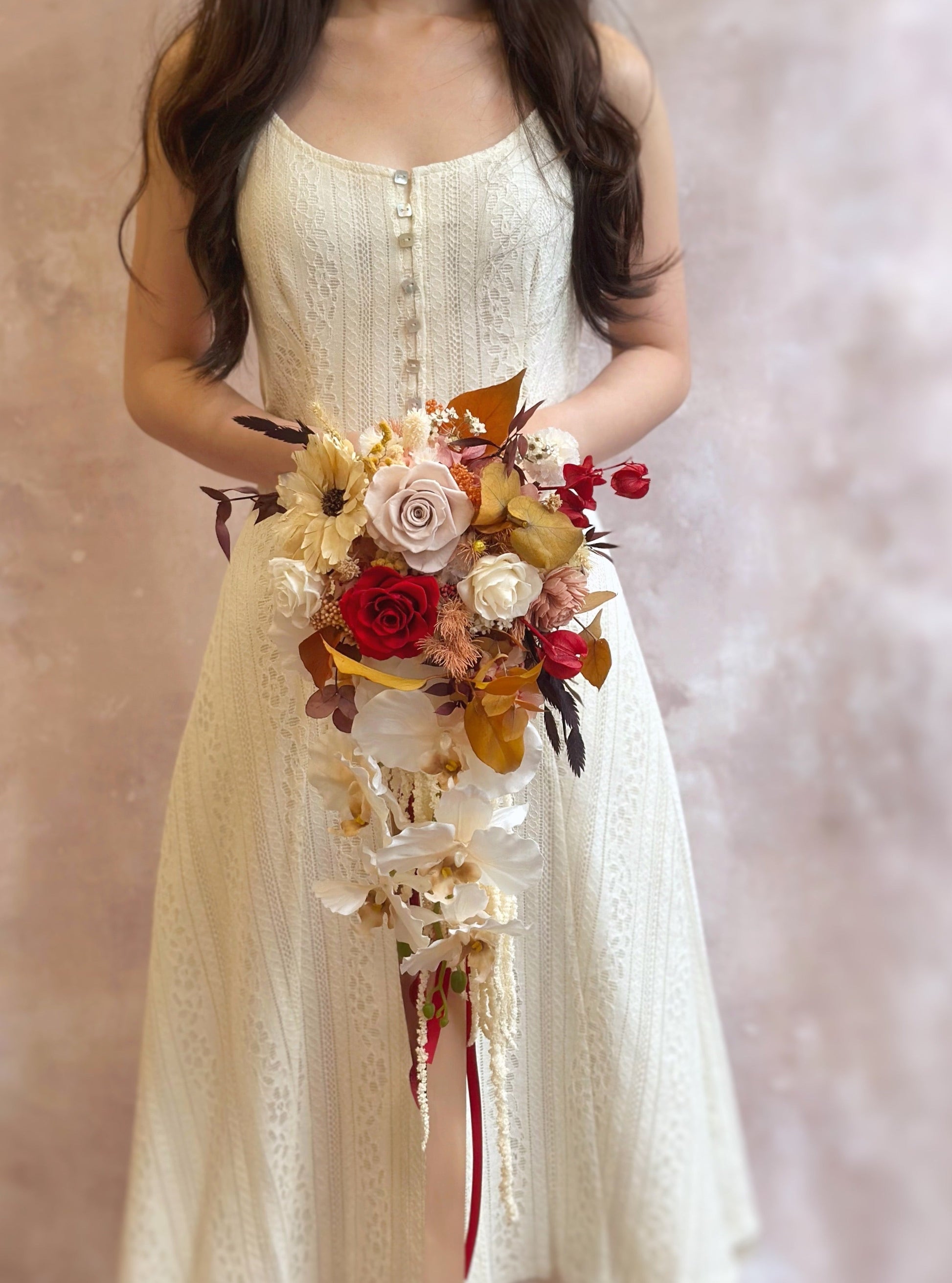 A bride holding the autumnal teardrop bouquet, its cascading florals and ribbons adding an ethereal, flowing effect.
新娘手持秋日泪滴型捧花，垂坠花材与丝带增添飘逸梦幻感。