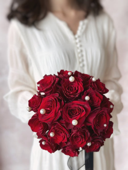 A model holding a bold maroon rose bouquet, adorned with pearls and a black ribbon for a striking and elegant look, close up view.
东方风情新娘捧花，深酒红玫瑰与珍珠装饰，尽显贵族气息


