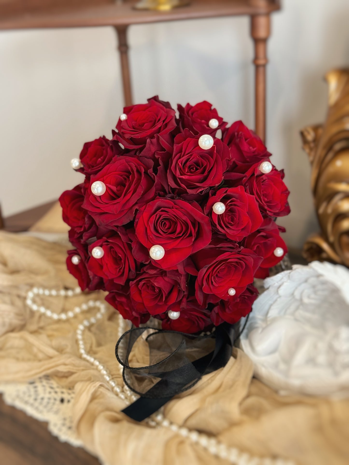 Fresh red Kenyan roses in round shaped for wedding close up view, a luxurious round bouquet of maroon roses elegantly adorned with pearls and a black ribbon, displayed on a table
经典圆形新娘捧花，深酒红玫瑰点缀珍珠与黑色丝带，华贵优雅
