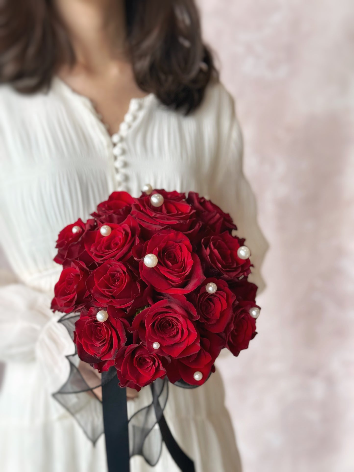 fresh red roses round bridal bouquet held by a model front view, a sophisticated bridal bouquet of deep maroon roses, enhanced with pearls and a black ribbon, held by a bride
深酒红玫瑰与珍珠的华丽对比，塑造大气难忘的新娘风格

